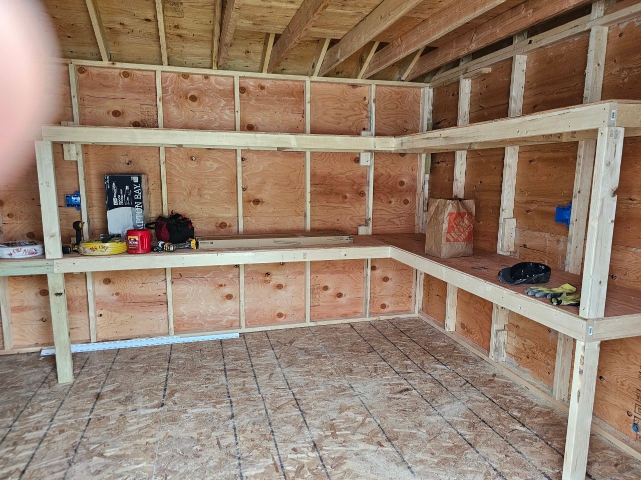 A wooden shed with shelves and a workbench in it.