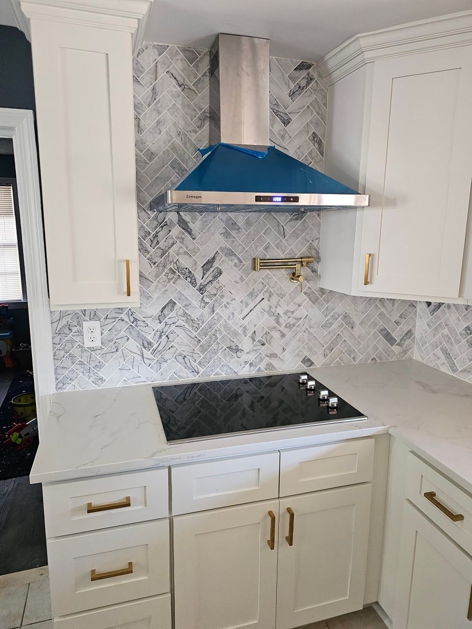 A kitchen with white cabinets , a stove top oven , and a blue hood.