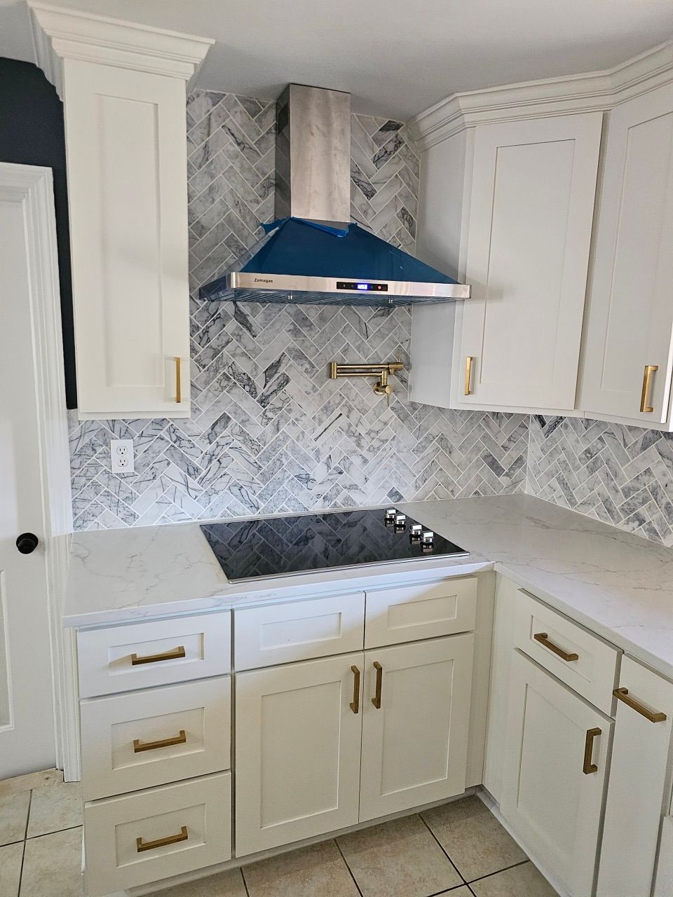 A kitchen with white cabinets , a stove top oven , and a blue hood.