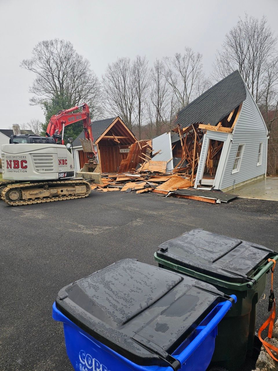 A house is being demolished with a bulldozer in the background.