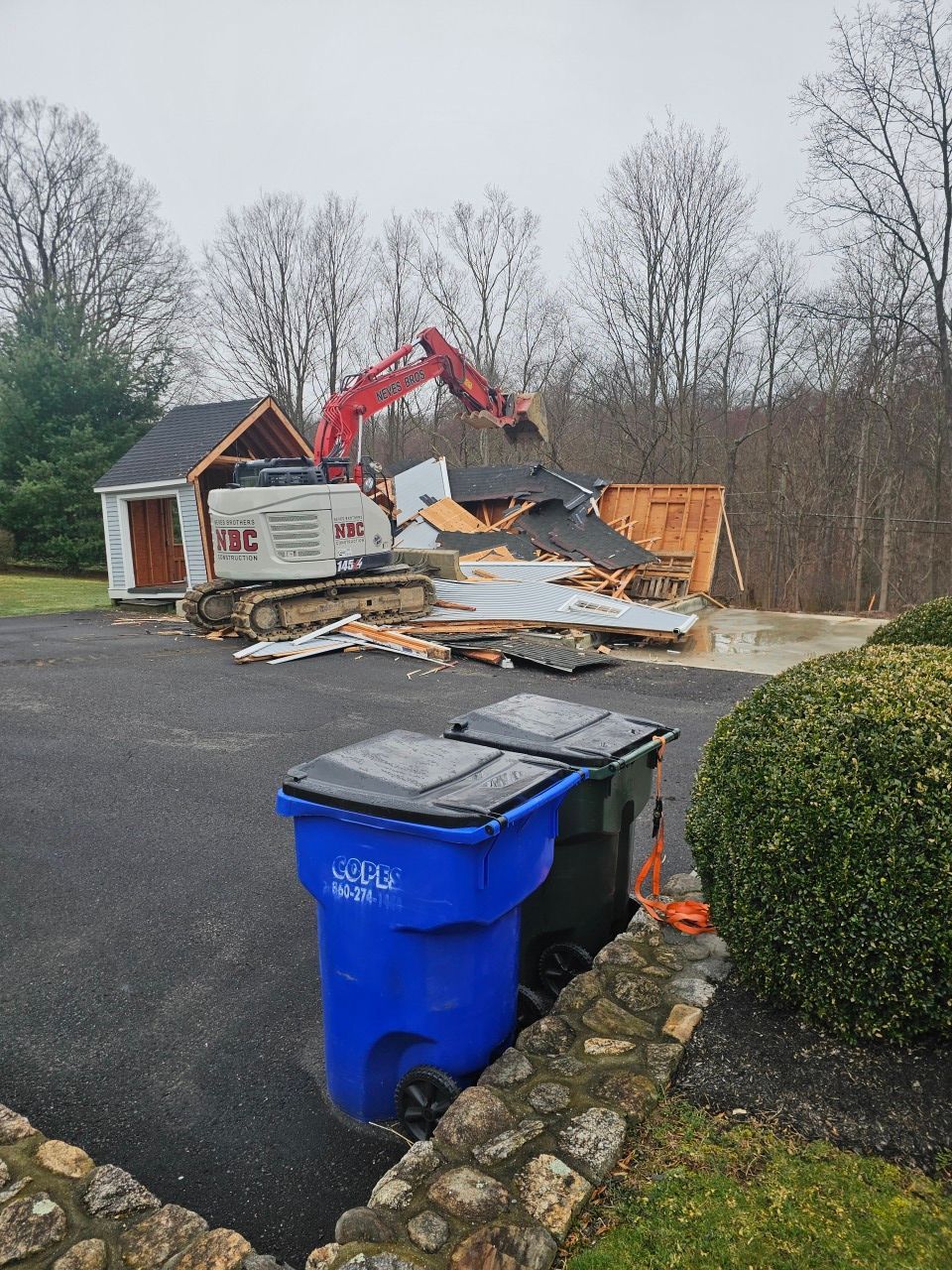 A blue trash can is sitting in front of a building being demolished.