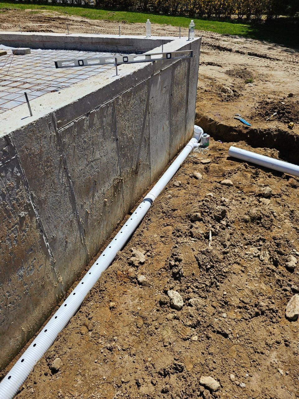 A white pipe is laying in the dirt next to a concrete wall.