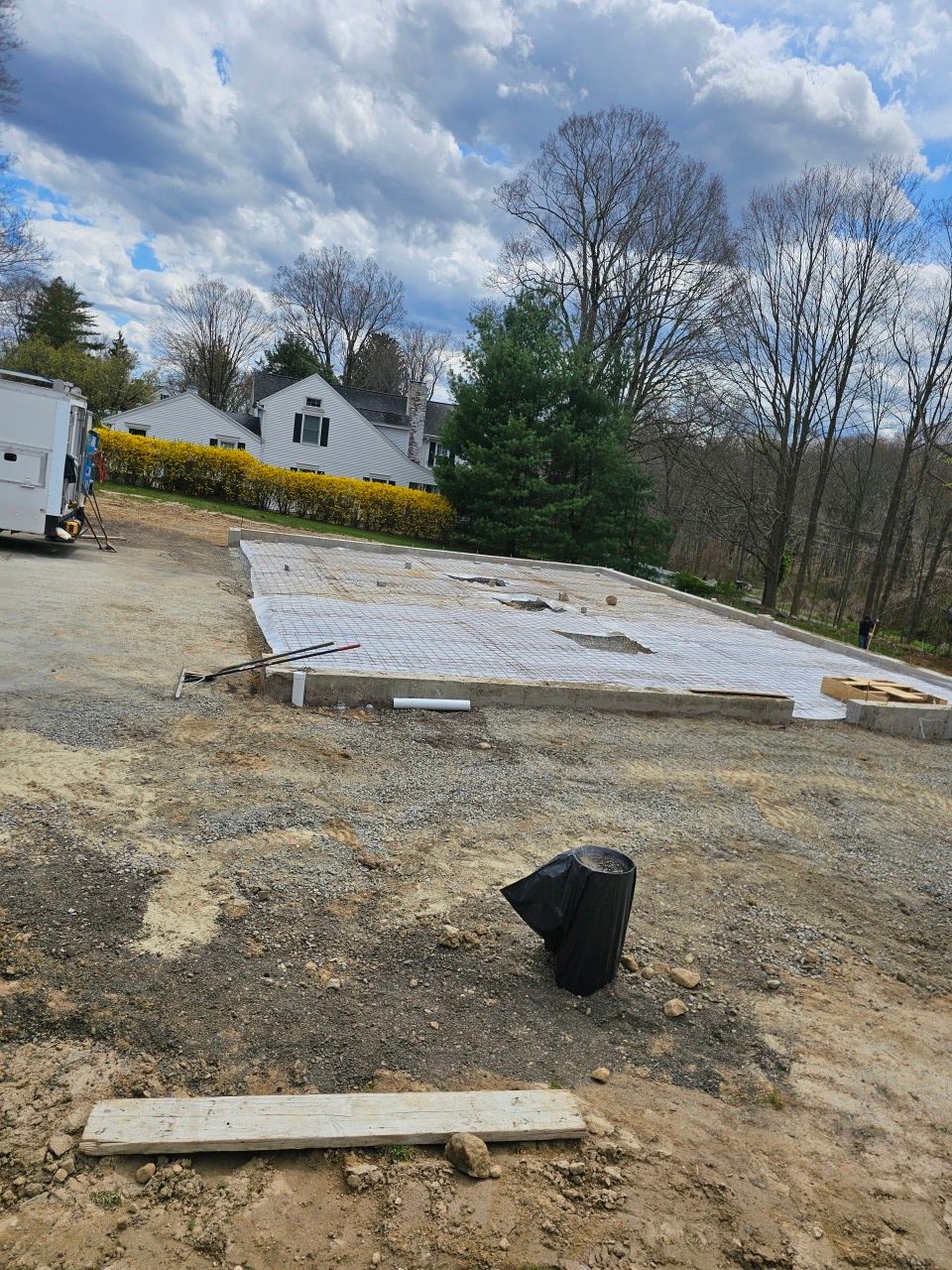A concrete foundation is being built in a dirt lot in front of a house.