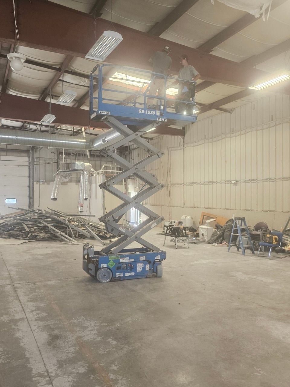 A man is standing on a scissor lift in an empty warehouse.