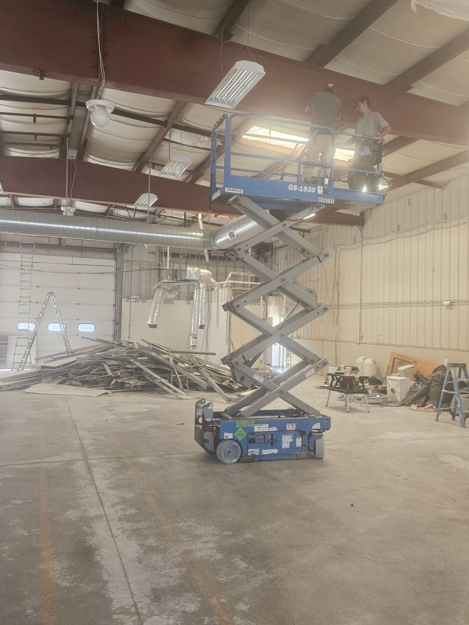 A man is standing on a scissor lift in a warehouse.