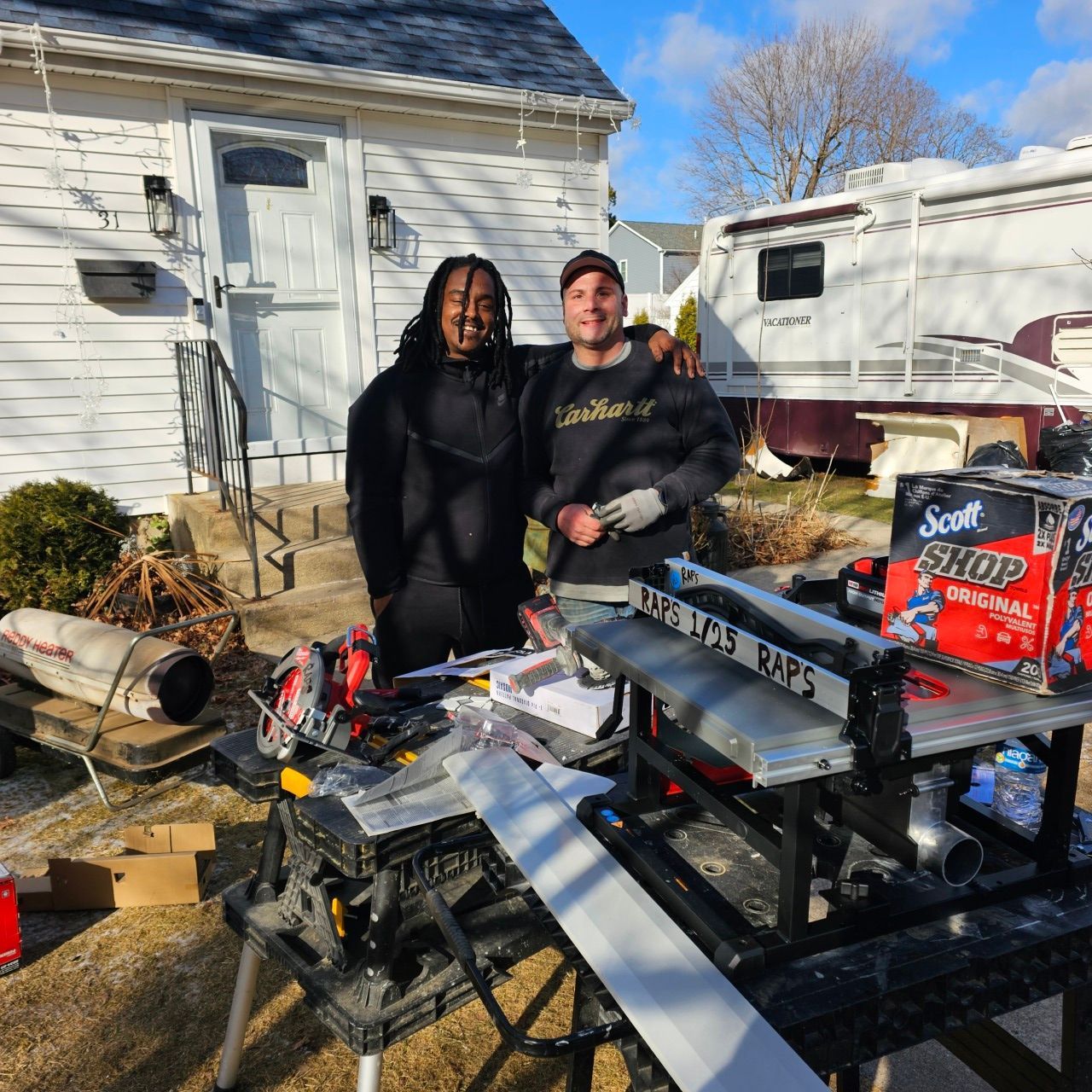 Two men are posing for a picture in front of a box of scott paper towels