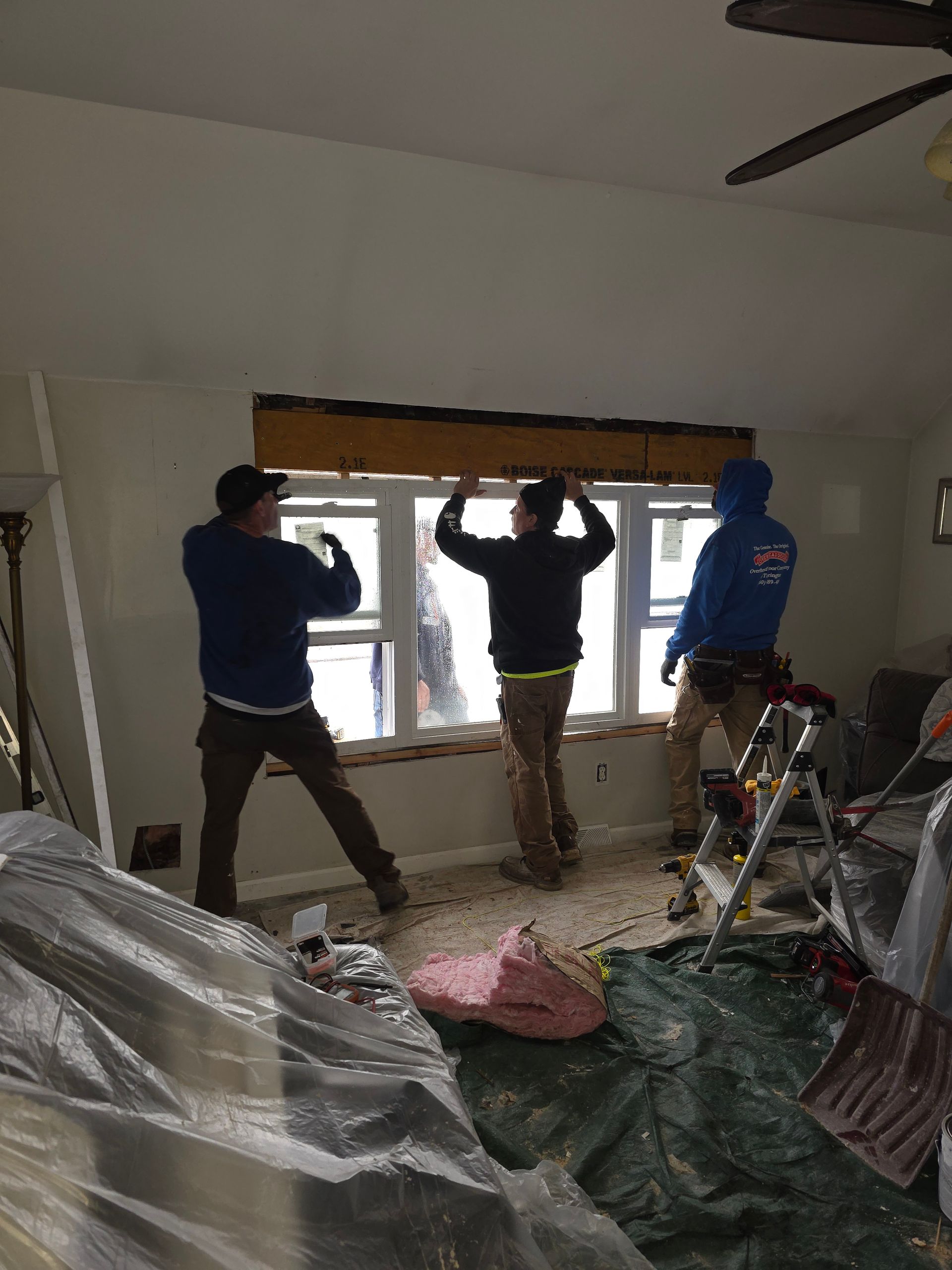 Three men are working on a window in a living room.