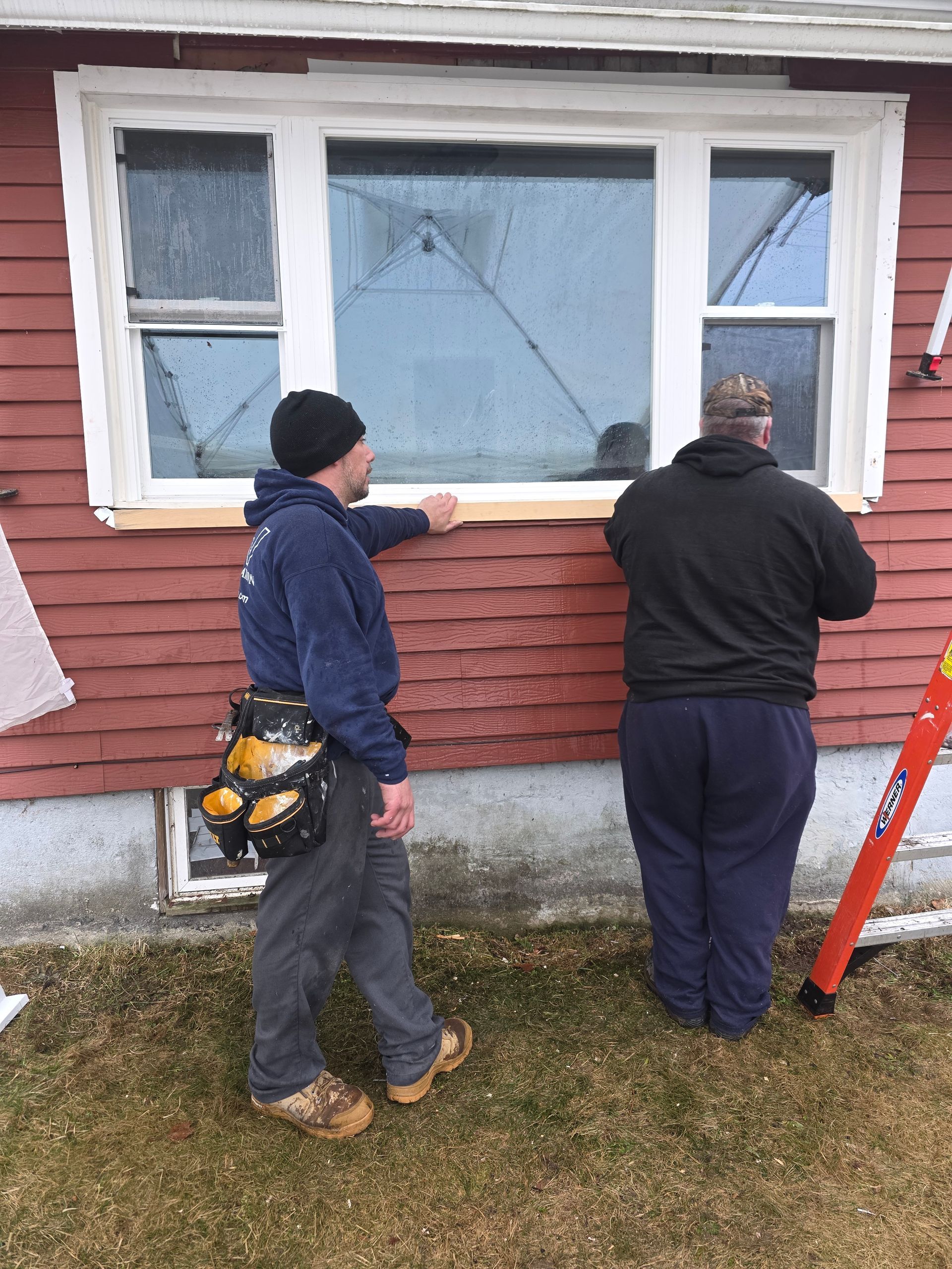 Two men are working on a window on the side of a house.