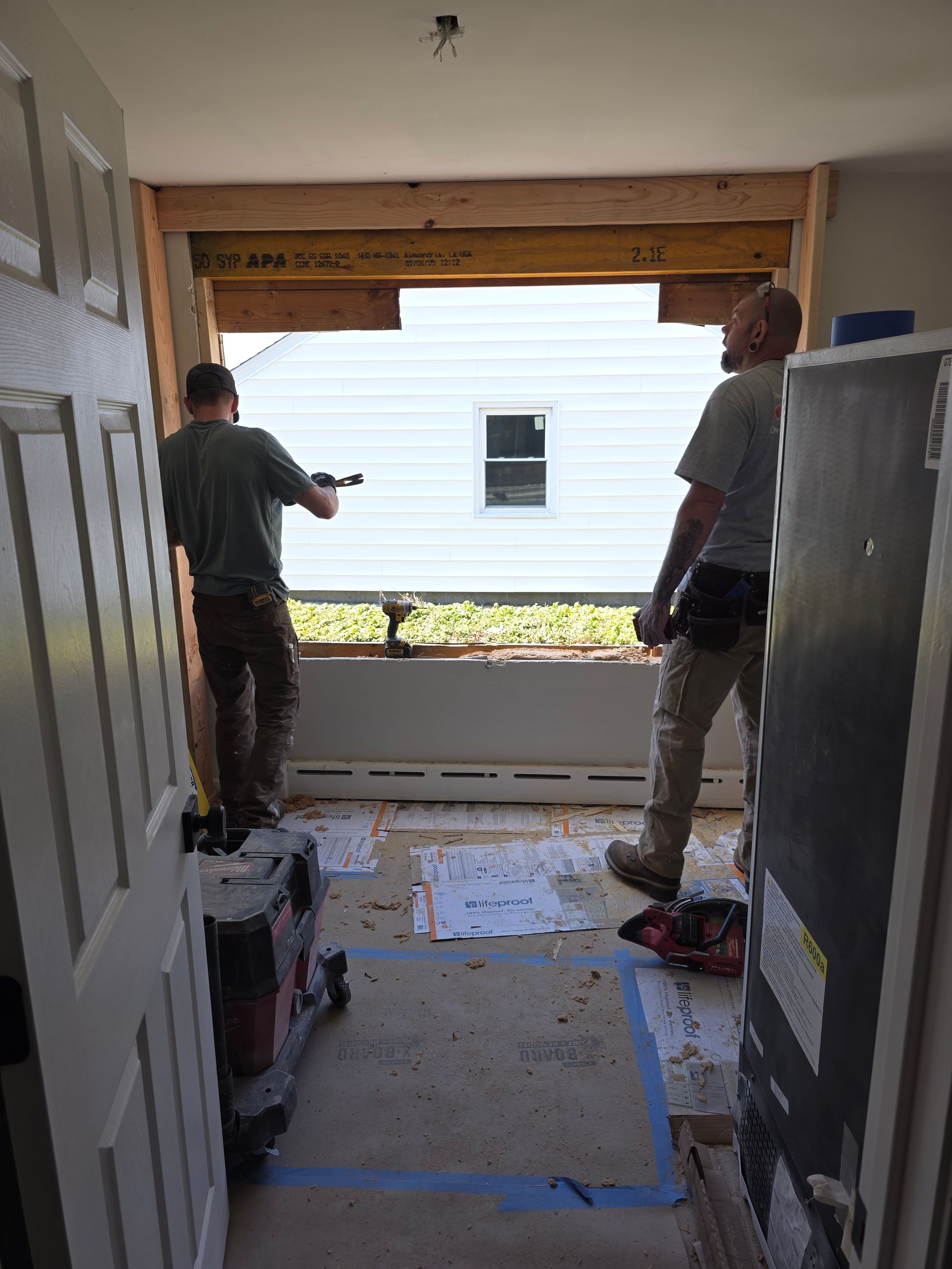 Two men are working on a window in a room.