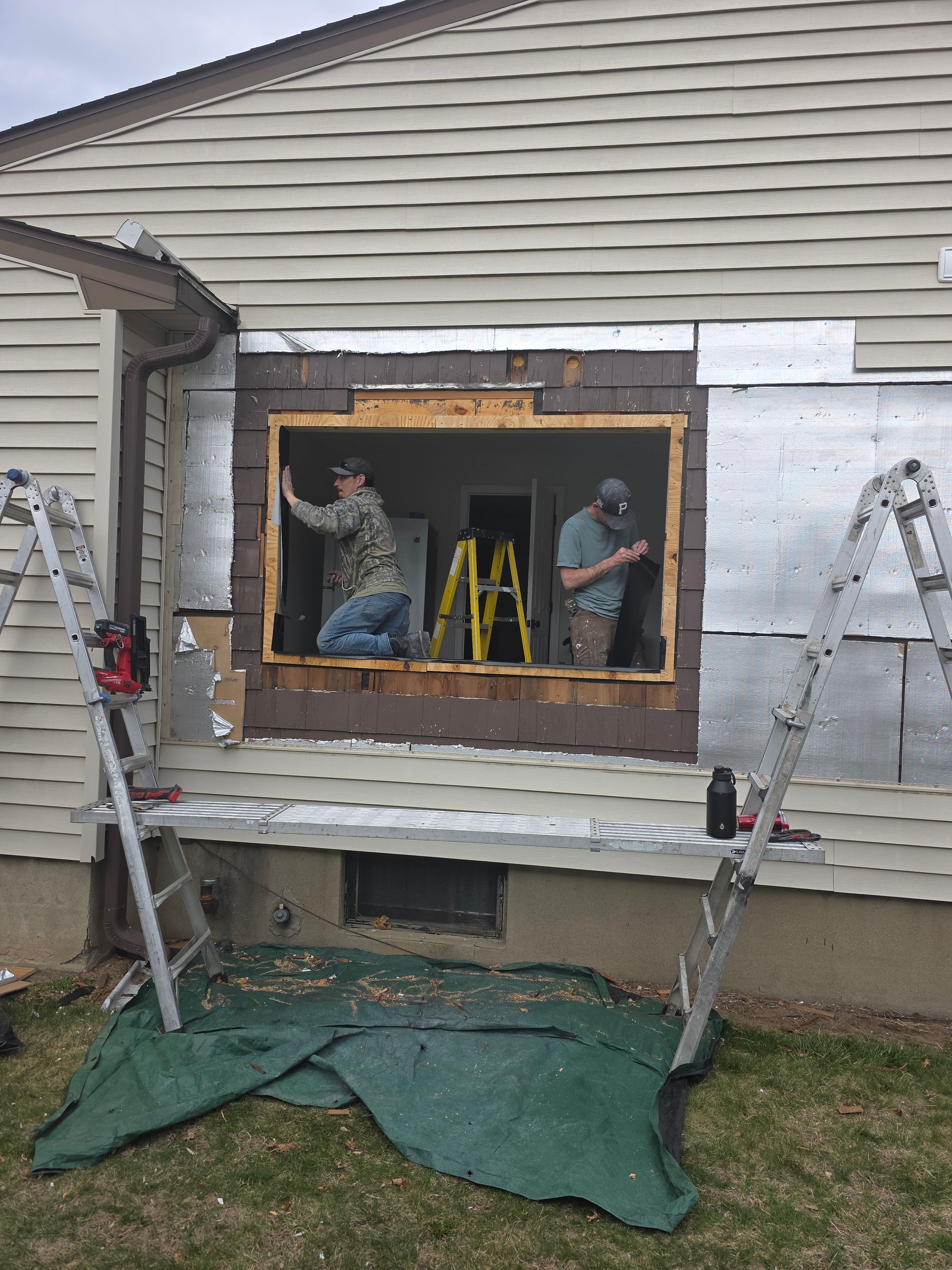 Two men are working on a window on the side of a house.