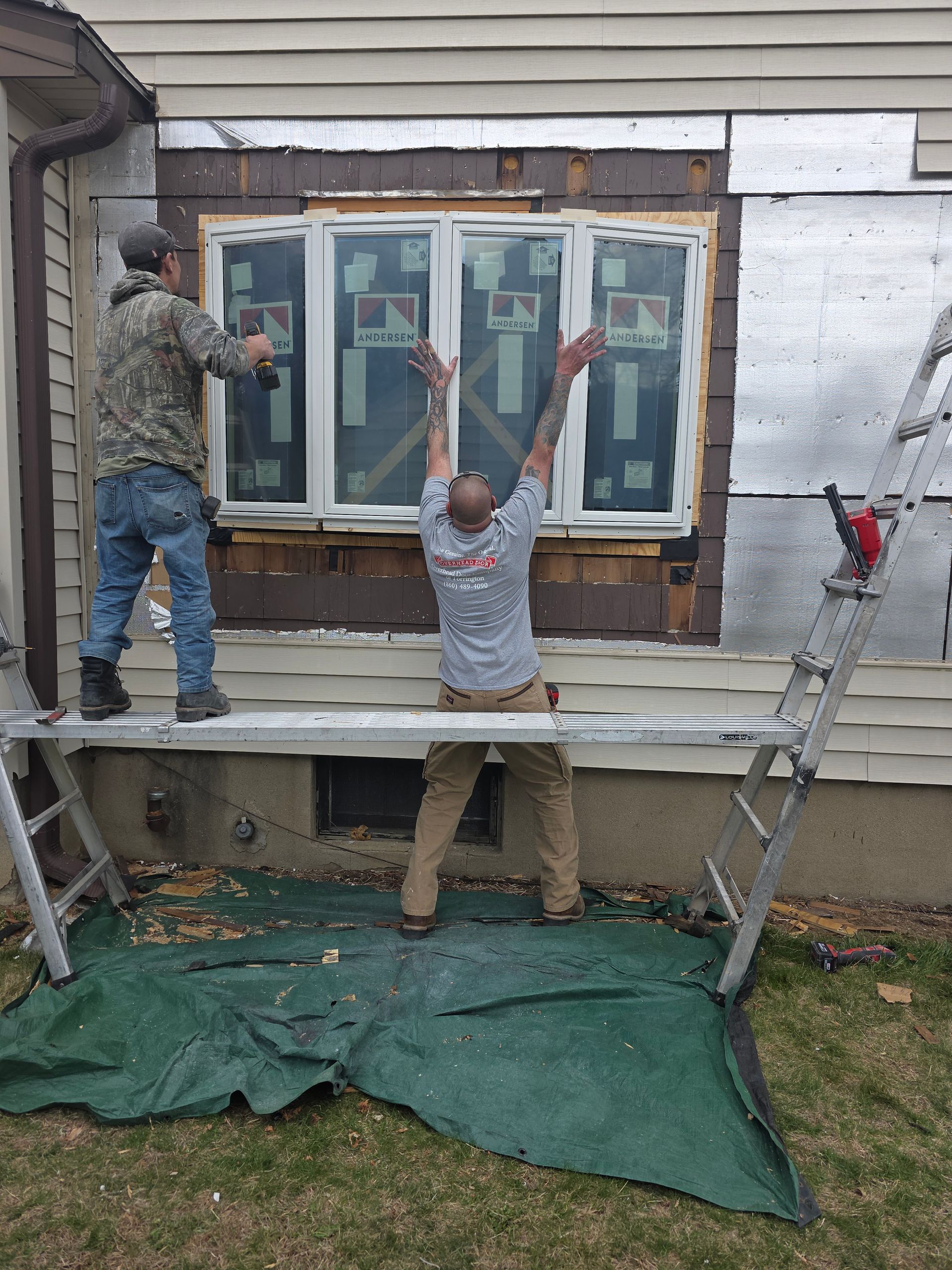 Two men are working on a window on the side of a house.