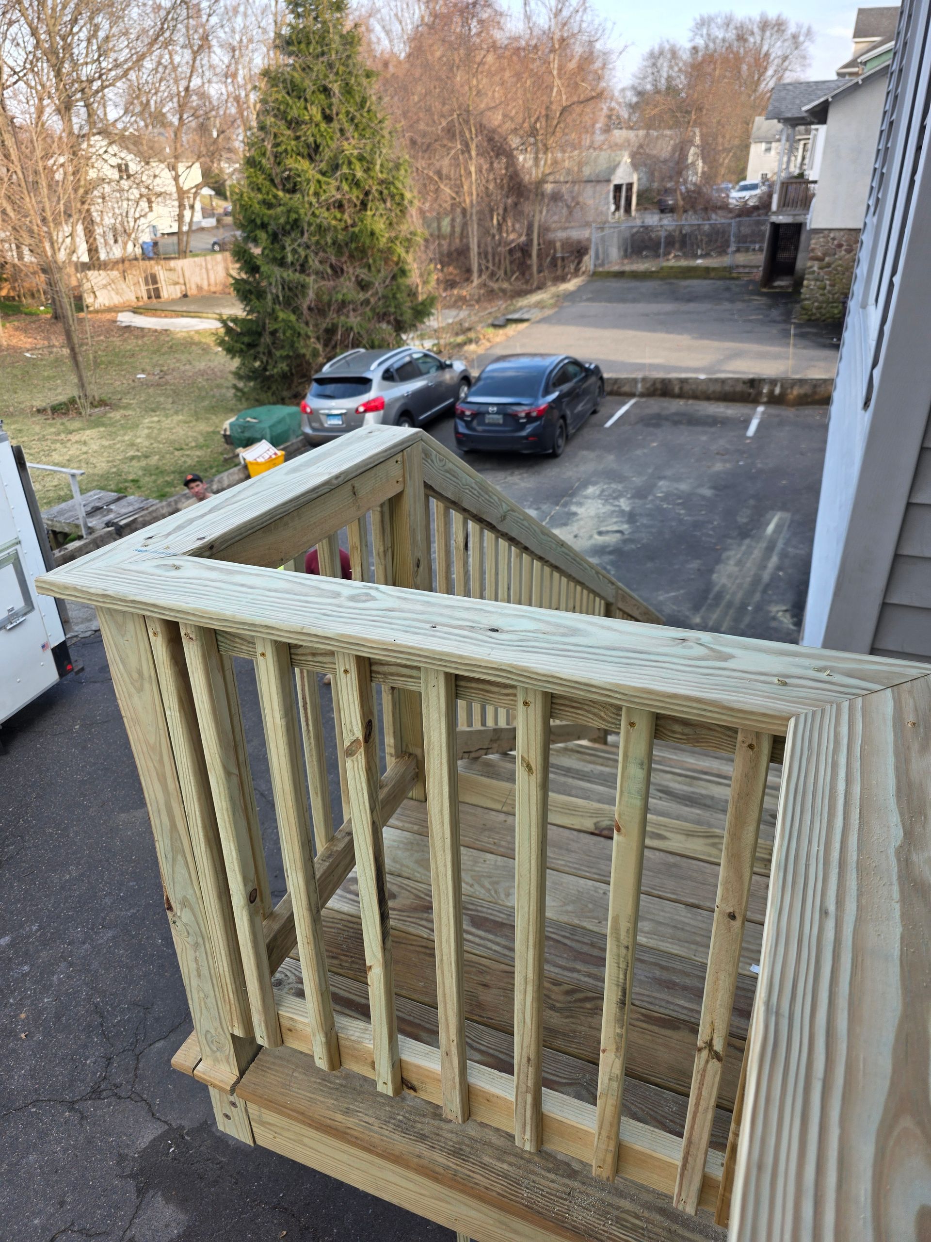 A wooden deck with stairs leading up to a parking lot.