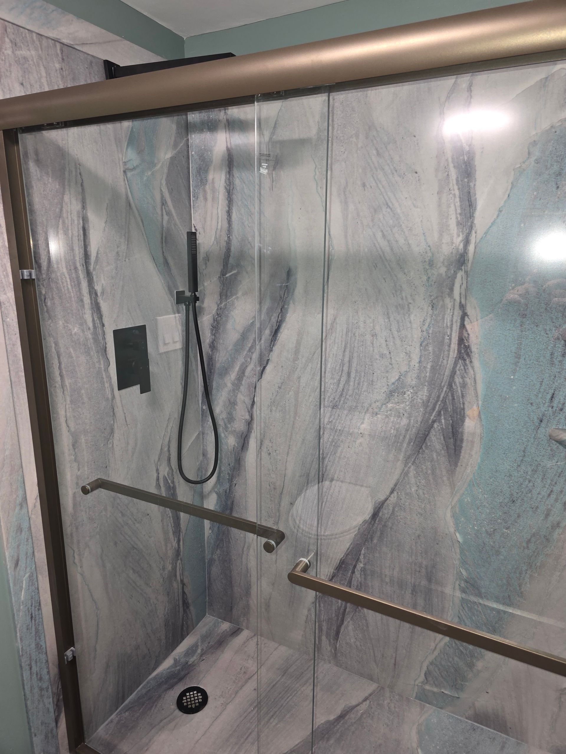A shower stall with a marble wall and sliding glass doors.