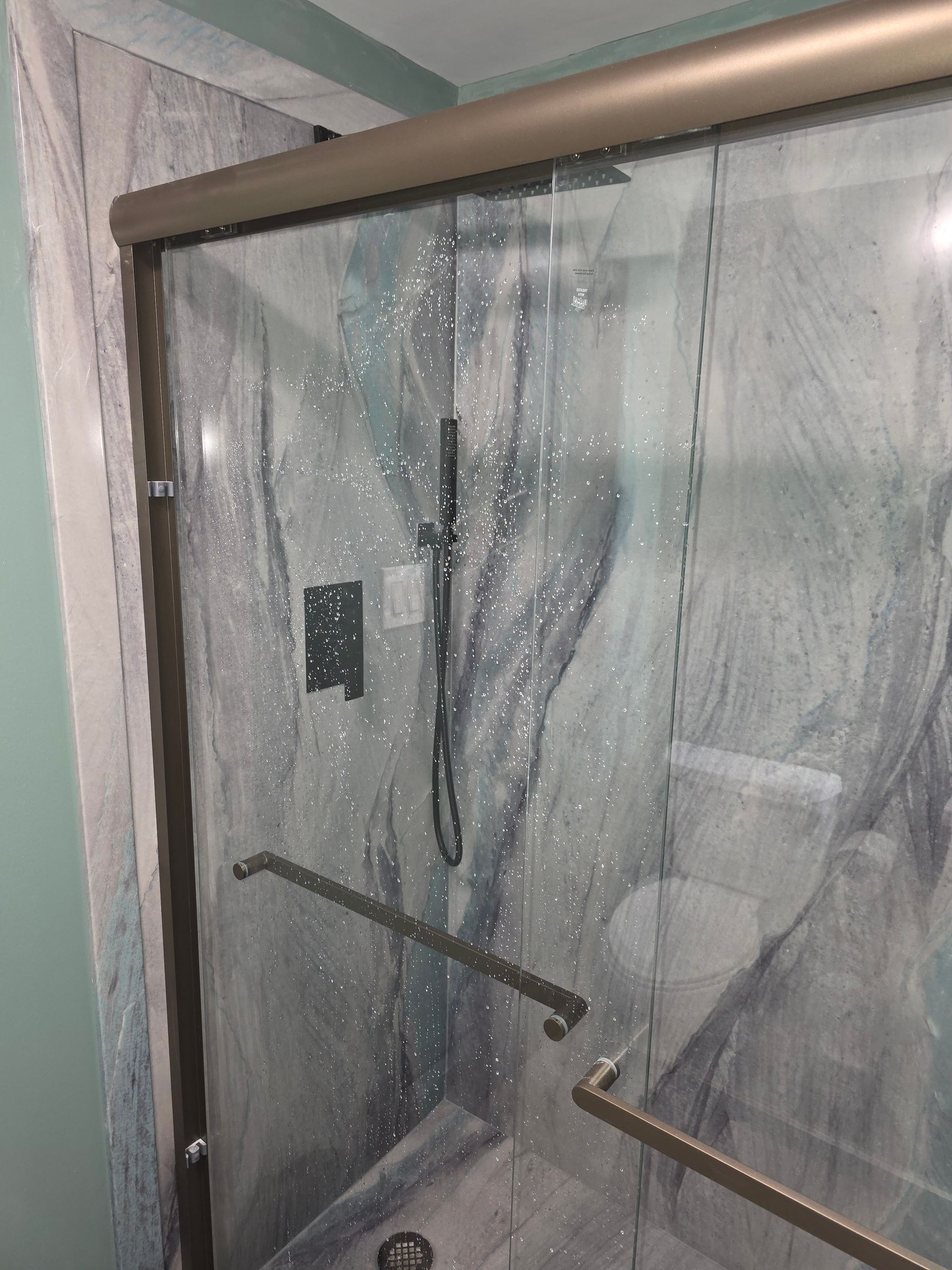 A shower stall with a sliding glass door and a shower head.