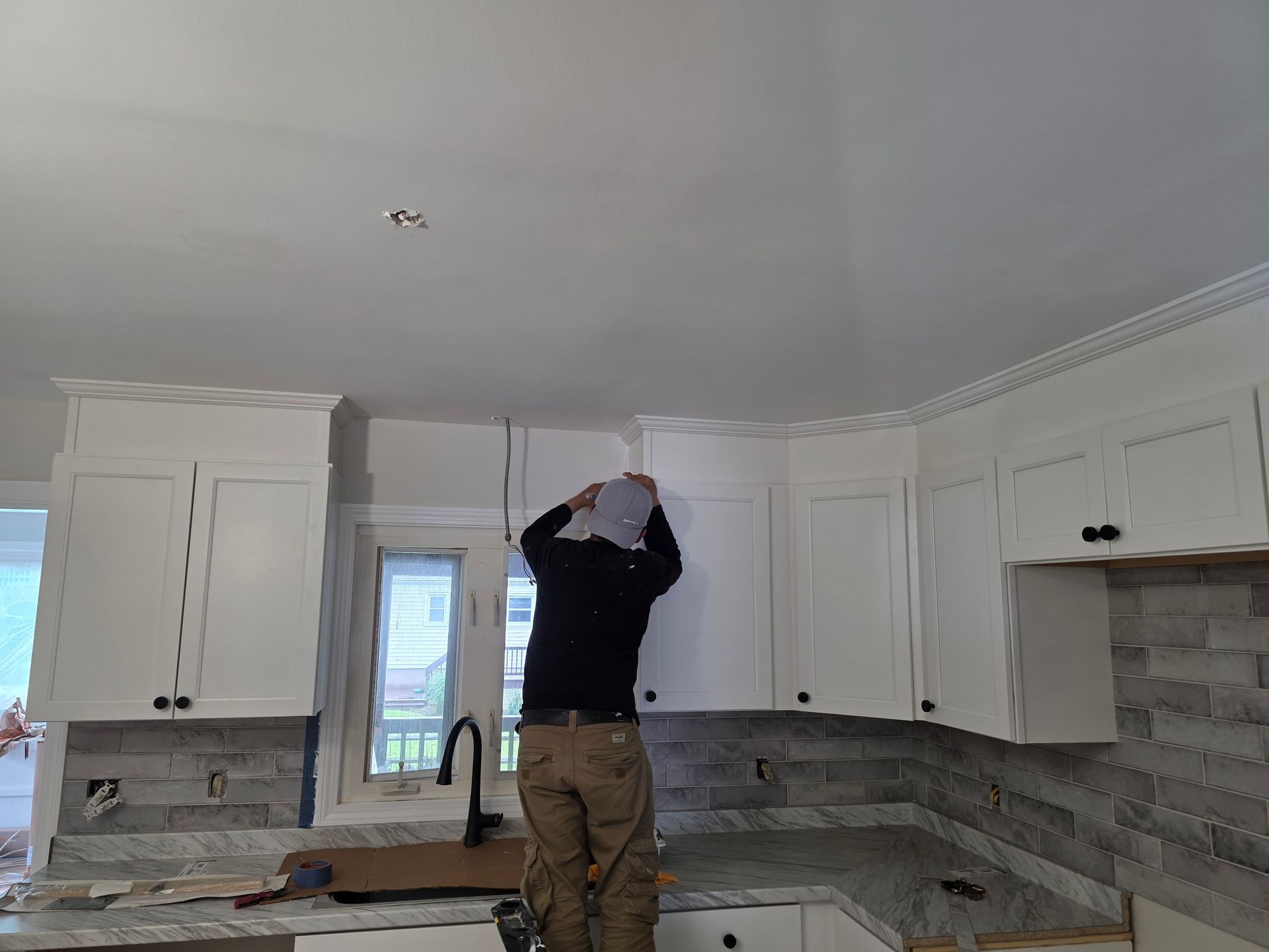 A man is standing in a kitchen looking up at the ceiling.