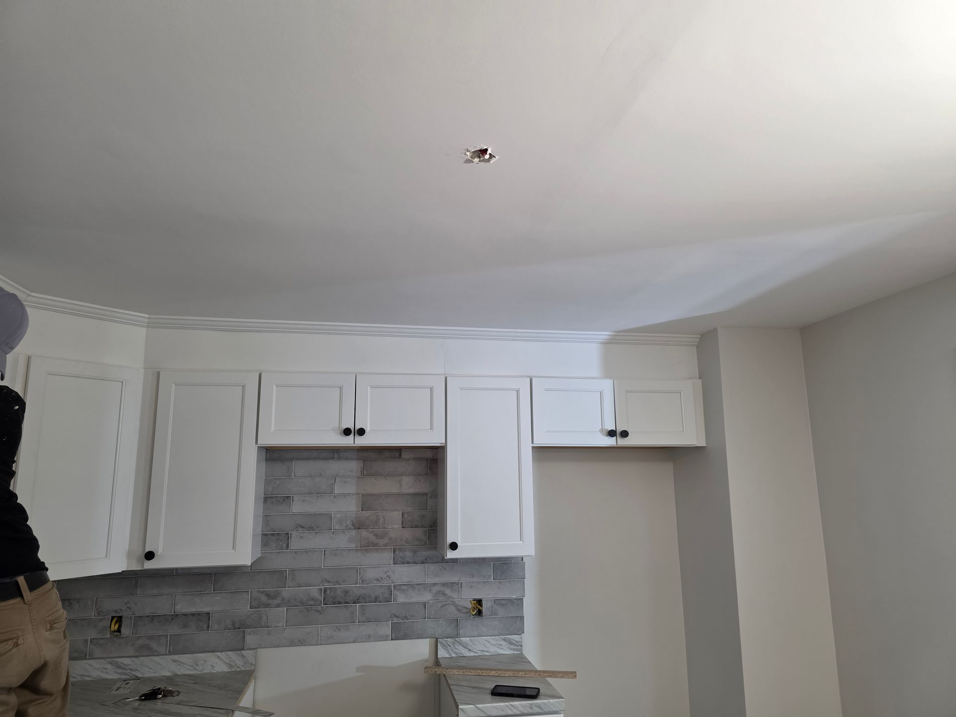 A kitchen with white cabinets and a ceiling that is being painted.