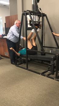 A man is helping a man do exercises on a machine.