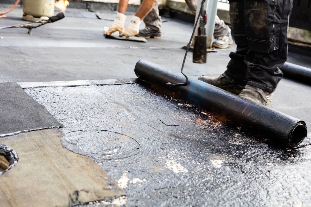 Worker Using a Torch to Seal a Roll of Sheet membrane on a Flat Roof — Consider It Sealed Waterproofing in Port Stephens, NSW
