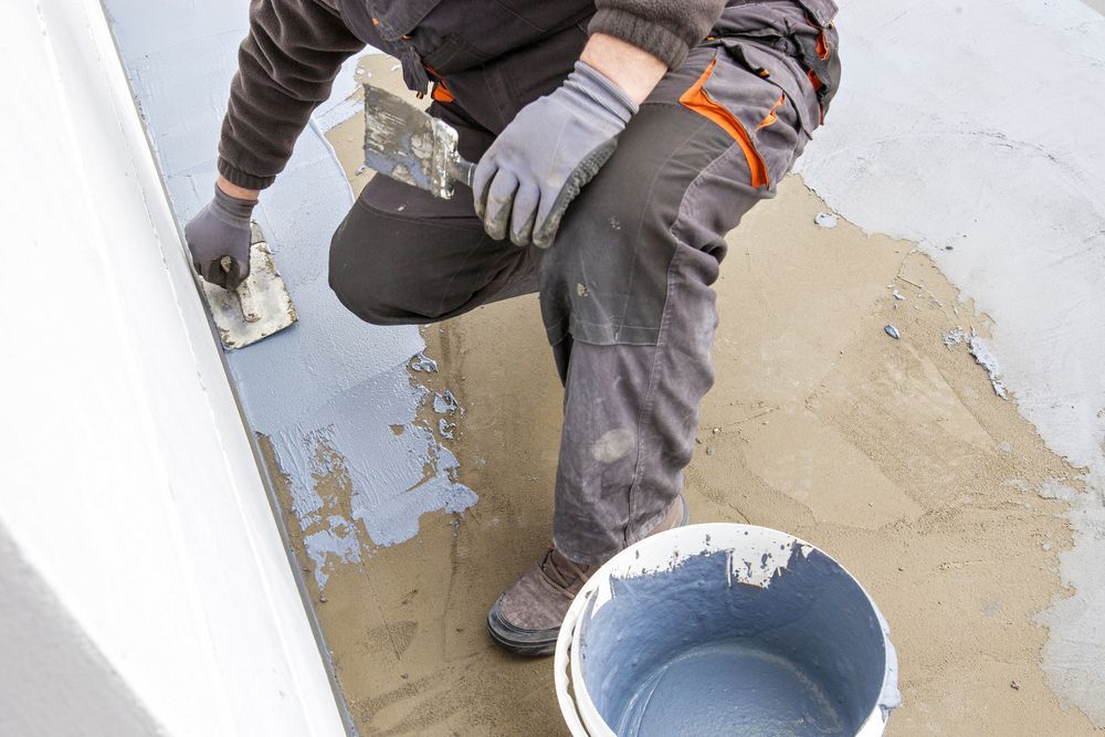 Person Applying Gray Sealant With a Trowel to a Concrete Surface — Consider it Sealed Waterproofing in Gosford, NSW