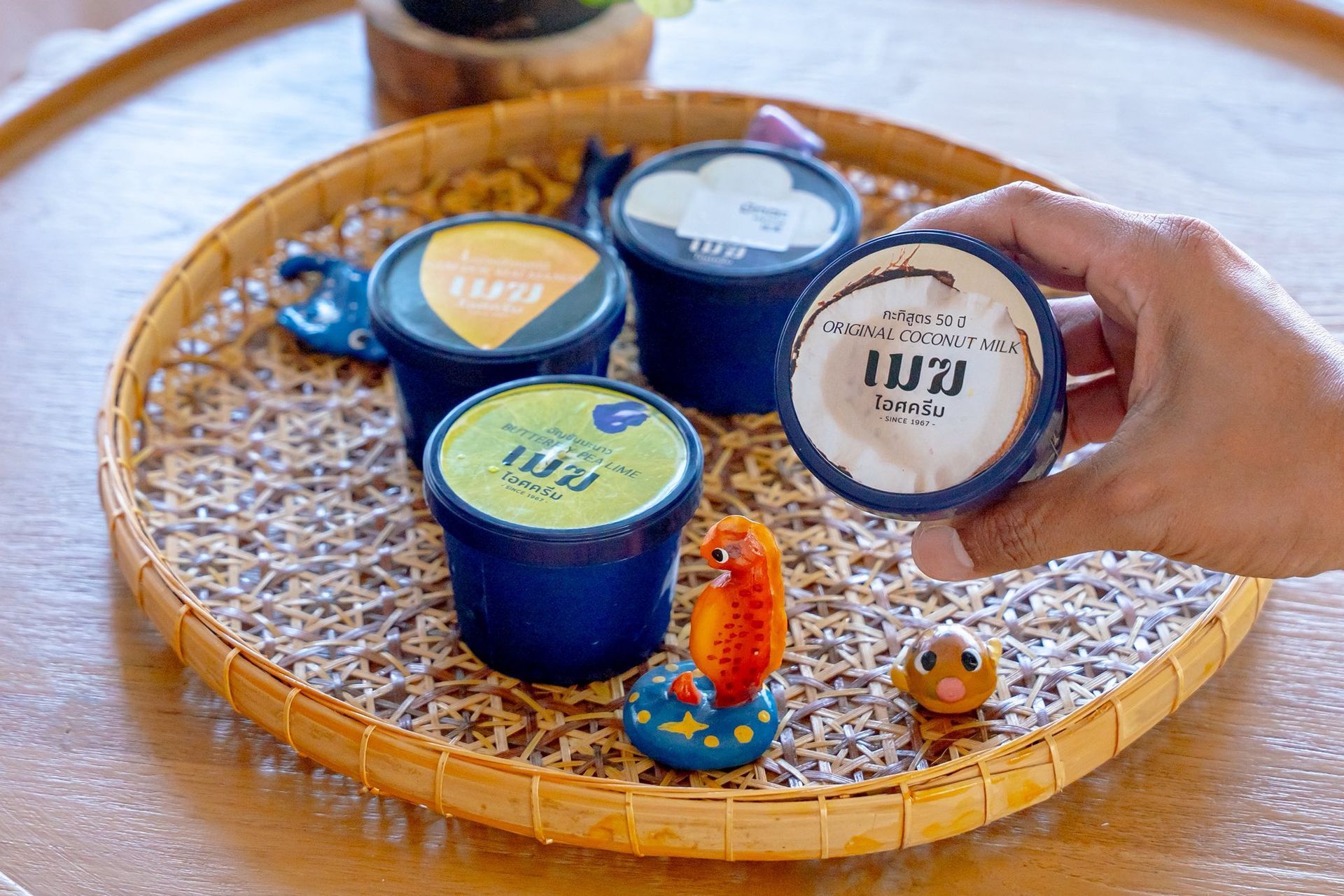 Tea set on woven tray with three blue cups and a hand holding a labeled container