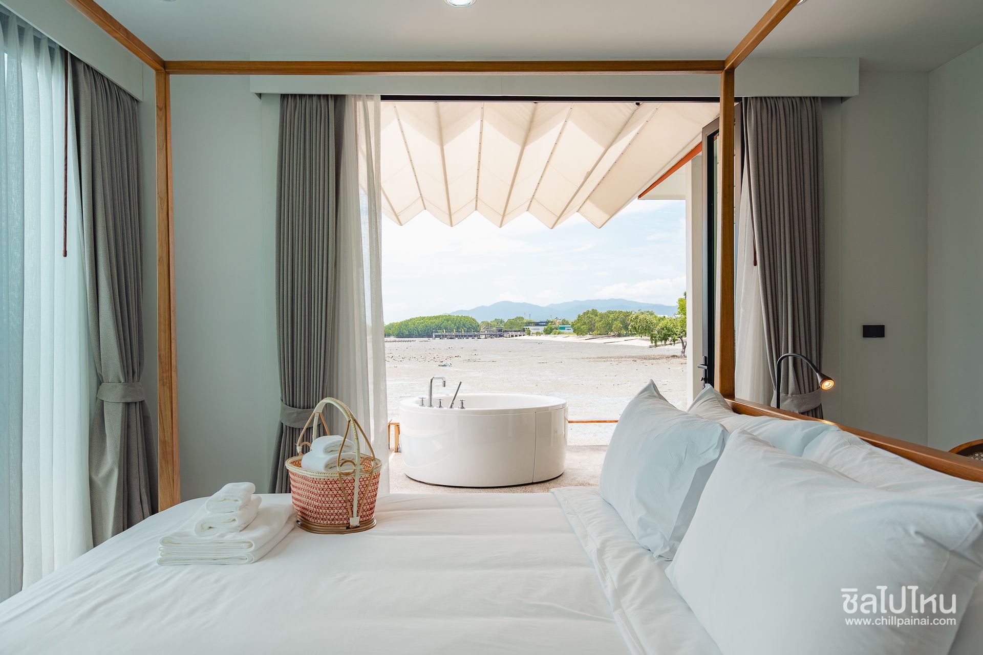 Bright bedroom with a large bed and open balcony view of a beach and mountains