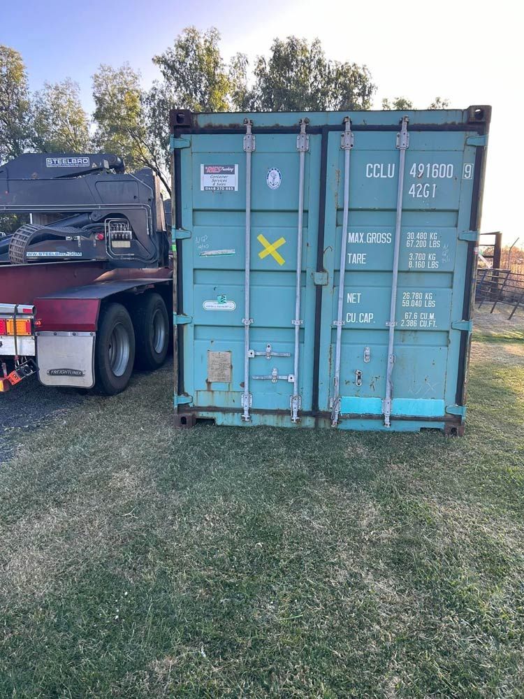 A Blue Shipping Container Is Parked in A Grassy Field Next To A Truck — Ries Trucking in Gowrie Mountain, QLD