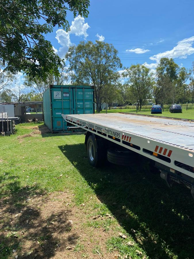 A Flatbed Tow Truck Is Parked In A Grassy Field Next To A Green Shipping Container — Ries Trucking in Gowrie Mountain, QLD