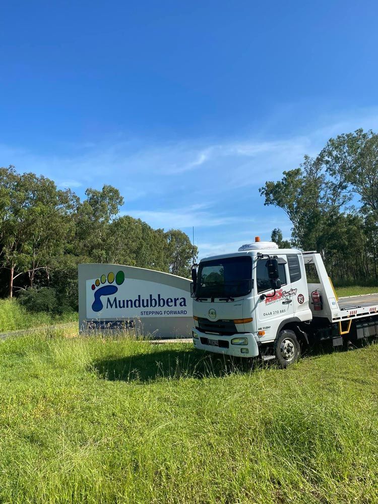 A Tow Truck Is Parked In A Grassy Field Next To A Sign — Ries Trucking in Gowrie Mountain, QLD