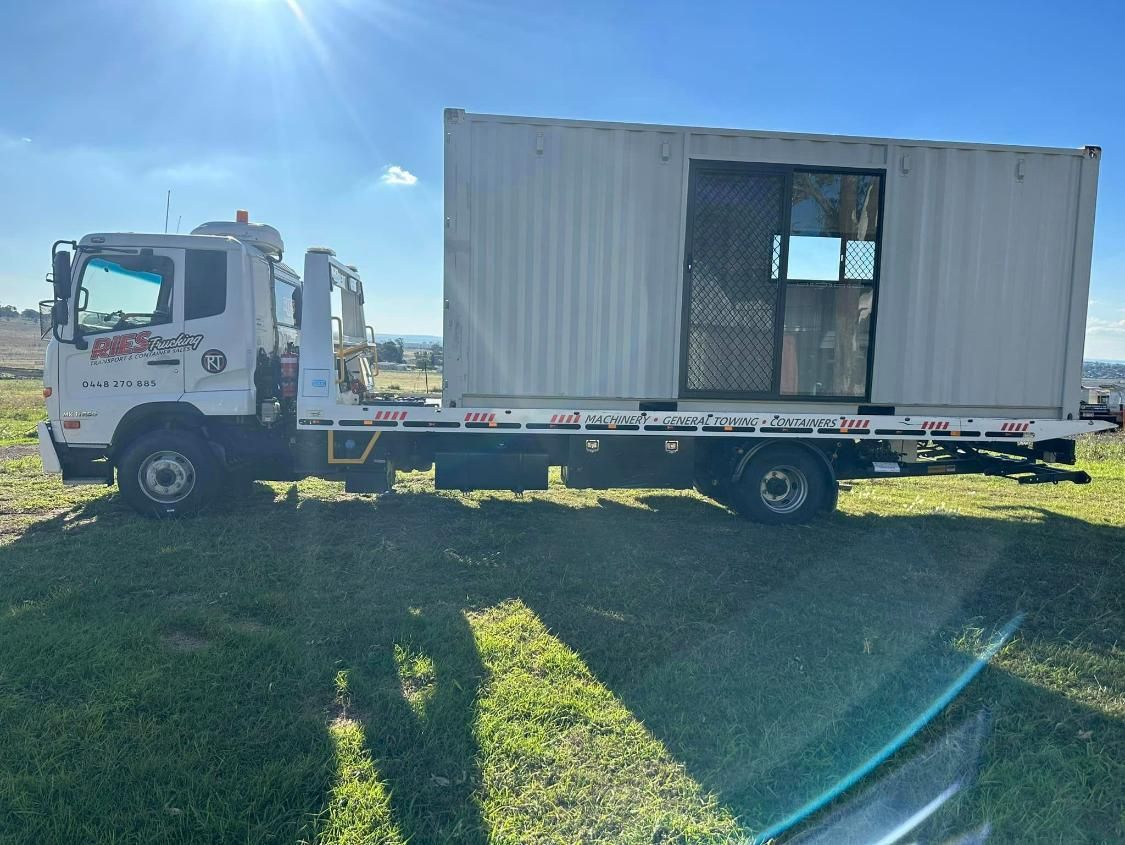 A Tow Truck Is Towing A Shipping Container In A Field — Ries Trucking in Chinchilla, QLD