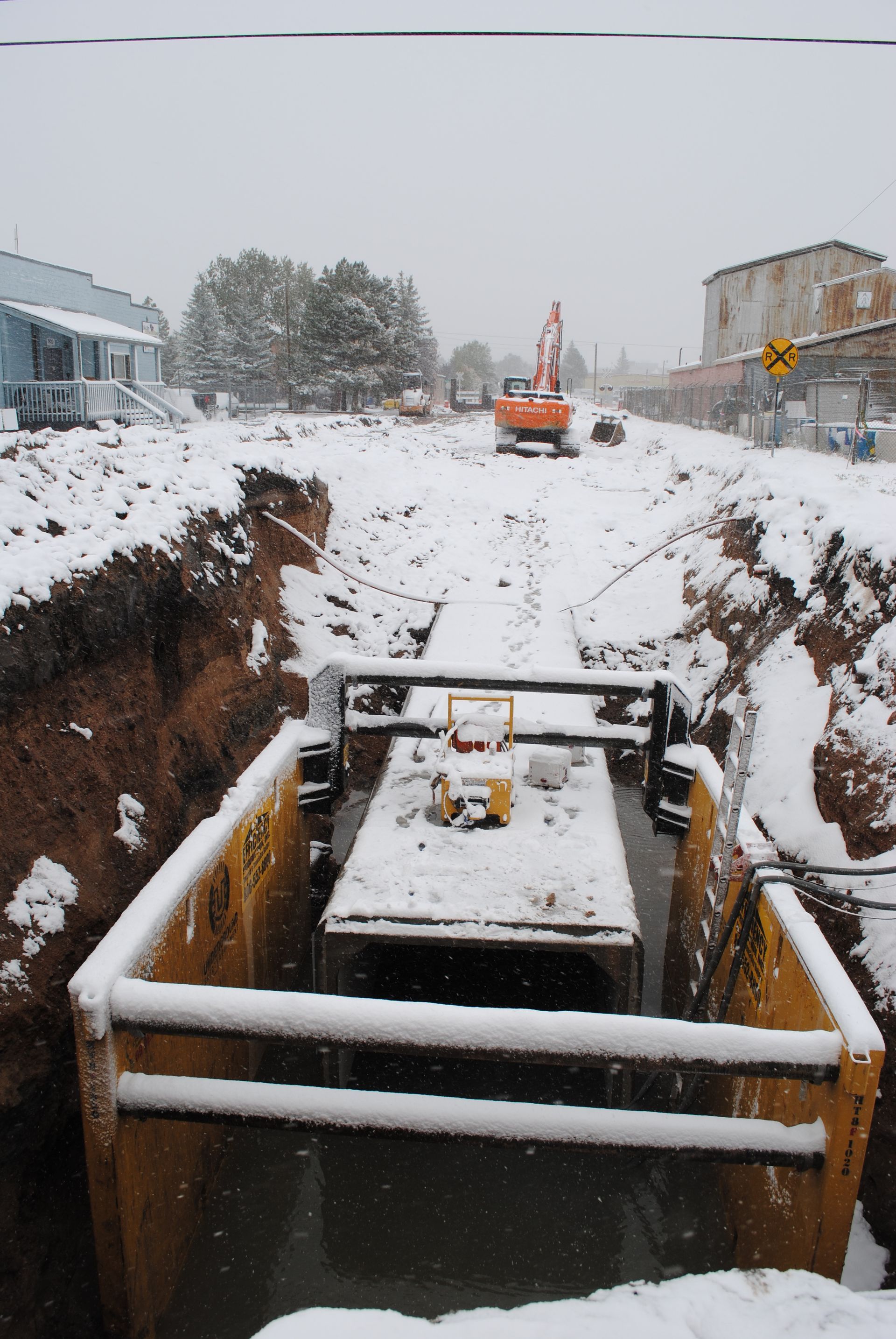 Snowy construction trench with an excavator and concrete structure in the foreground
