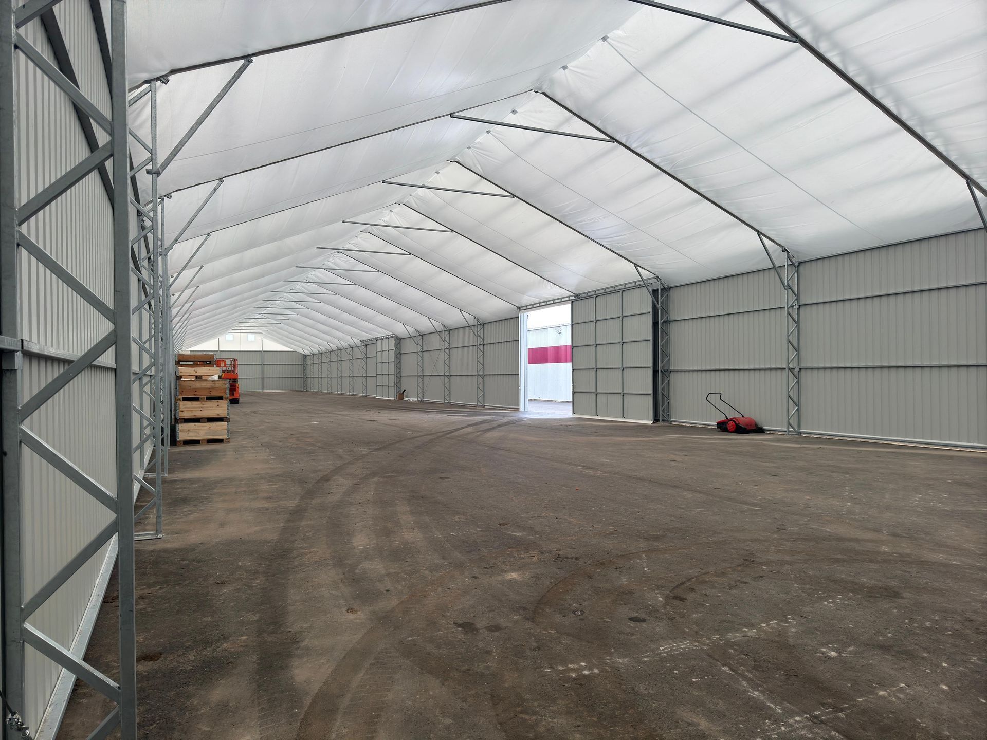 Didelės, tuščios baltos palapinės su purvinomis grindimis, metalinėmis atramomis ir atviromis durimis vidus.