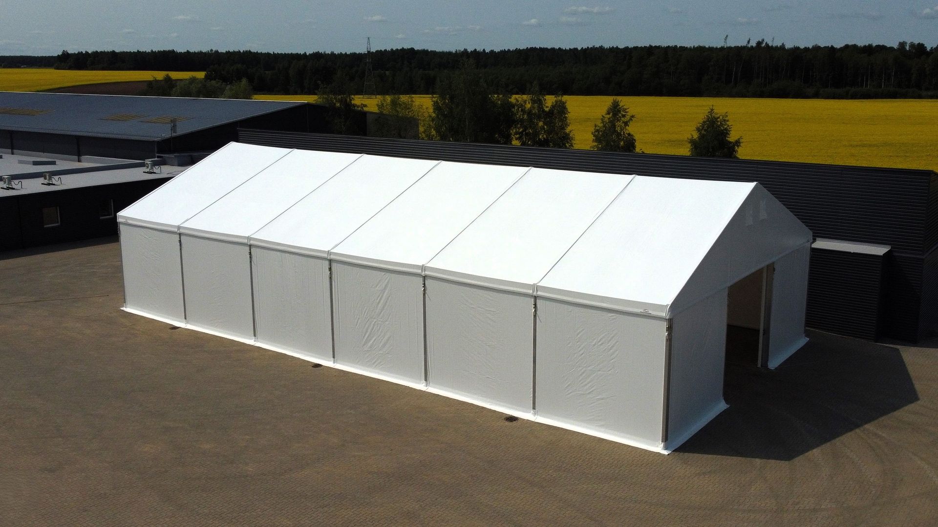 Balta stačiakampė palapinės konstrukcija su dvišlaičiu stogu atvirame lauke.