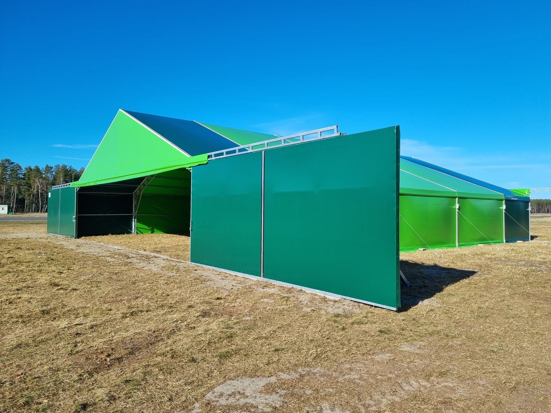 Žalia palapinės konstrukcija lauke po mėlynu dangumi.