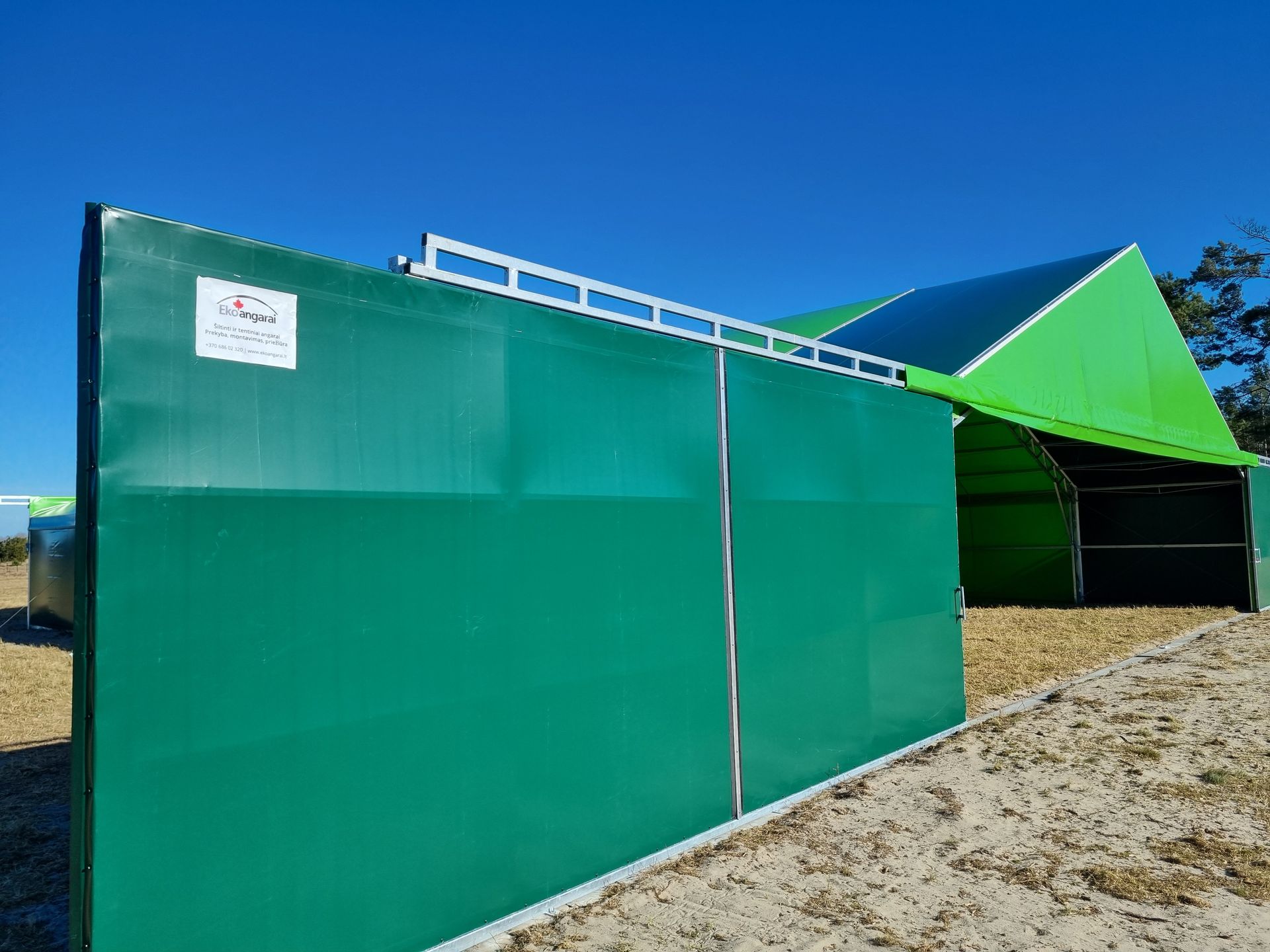 Žalia tvora priešais žalią statinį su baltu viršutiniu turėklu mėlyno dangaus fone.
