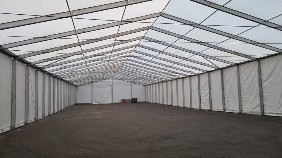 Didelės, tuščios palapinės su baltu stogu ir sienomis, pastatytos ant tamsios žemės, vaizdas iš vidaus.