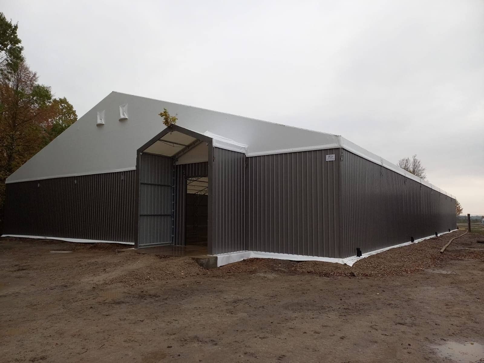 Pilkas metalinis pastatas su baltu stogu ir atviromis durimis lauke.