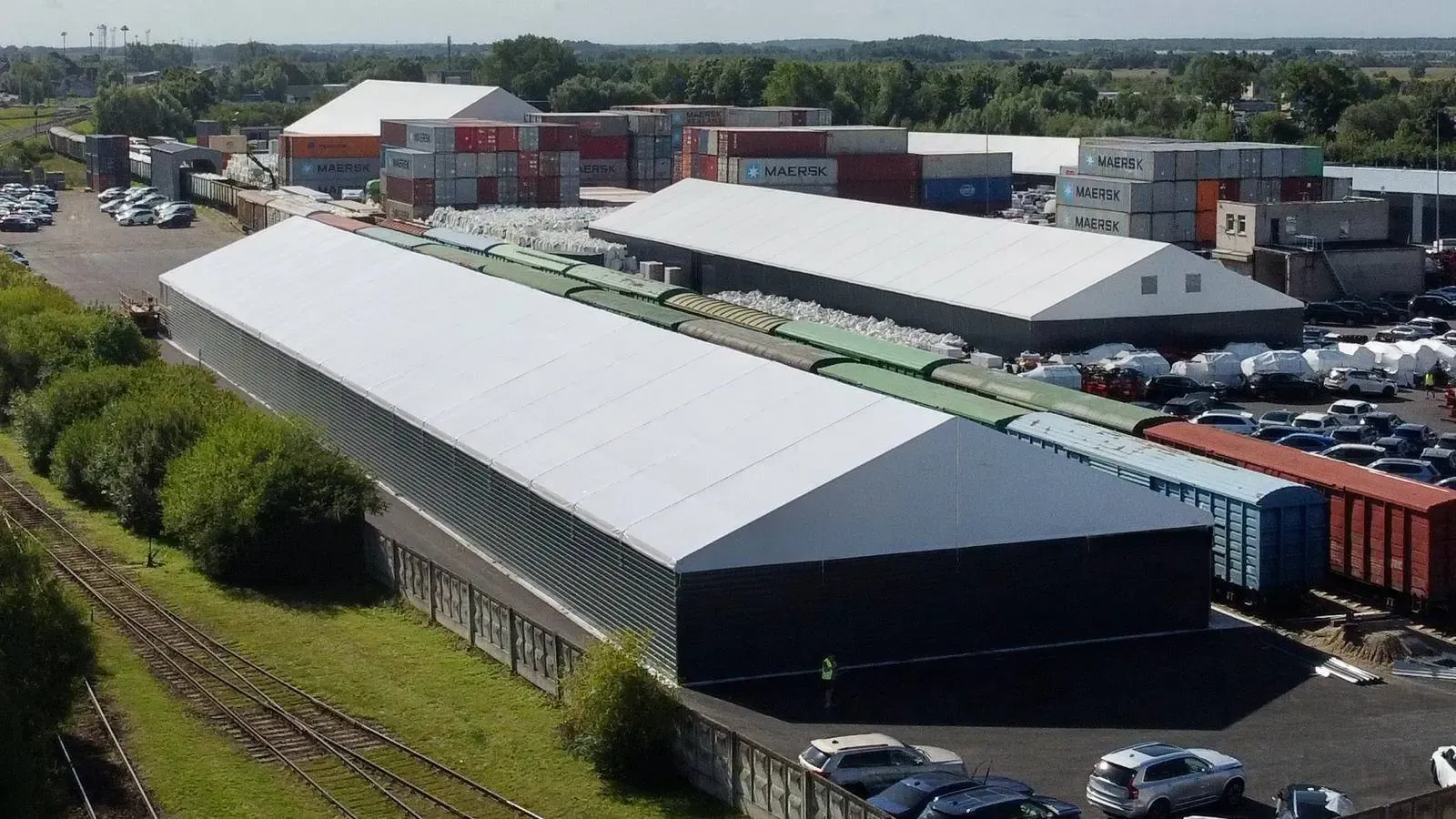 Sandėlis su gabenimo konteineriais ir geležinkelio vagonais saulėtą dieną.