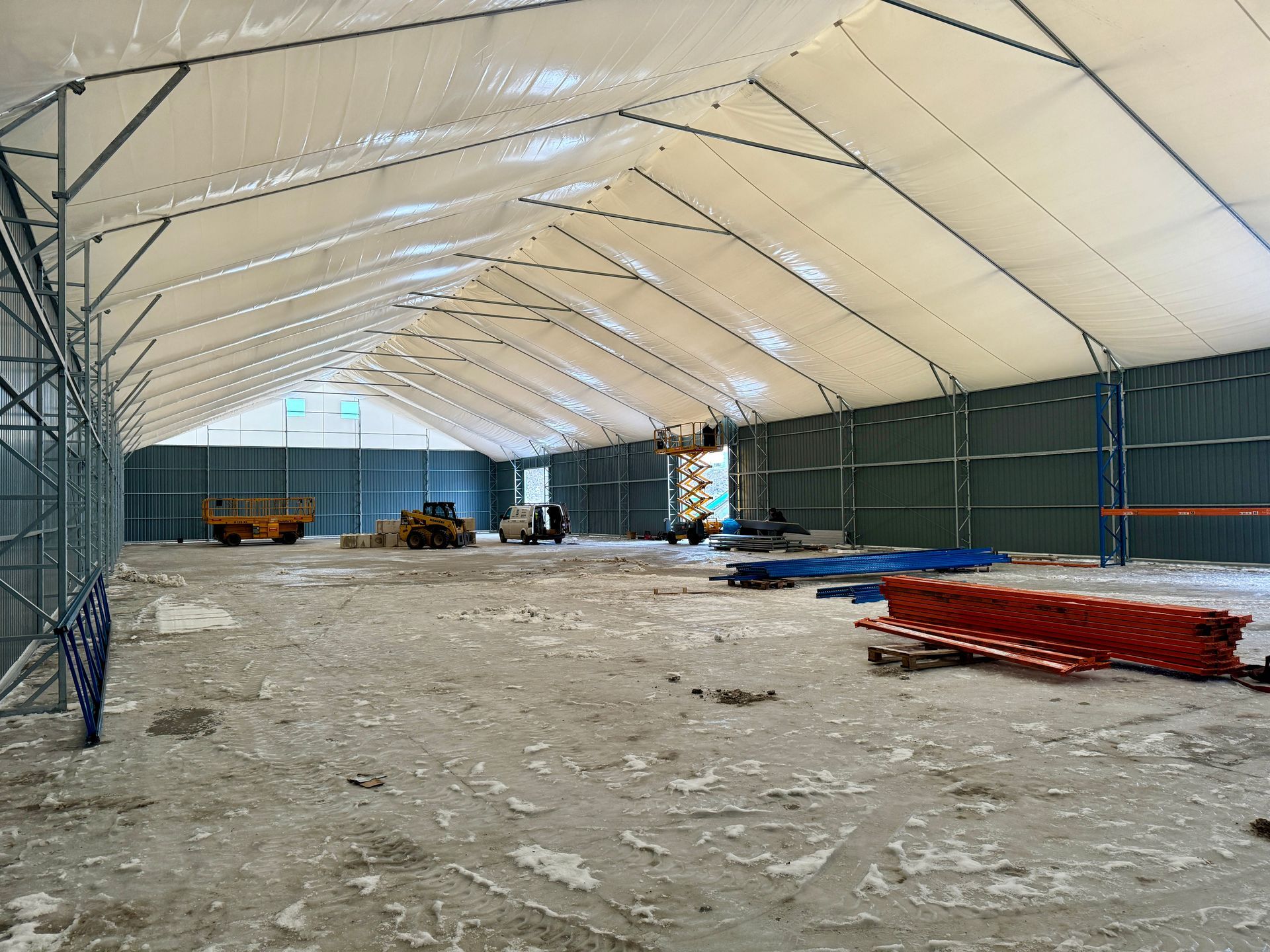 Didelės, tuščios palapinės su metaliniu karkasu vidus. Statybinė įranga ir nuolaužos ant žemės.