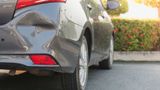 A car with a damaged bumper is parked on the side of the road.