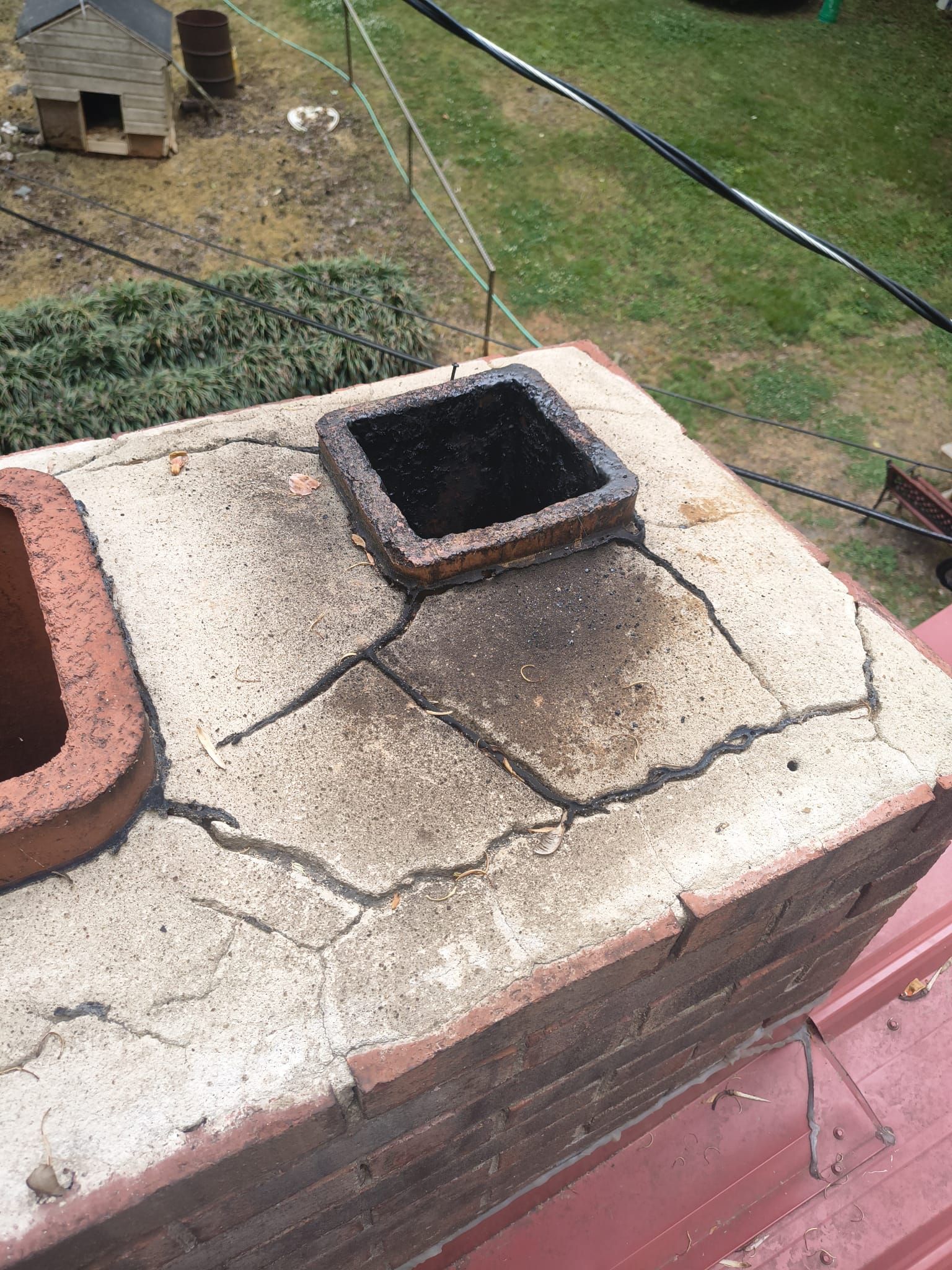 Weathered rooftop chimney with a square opening and cracked concrete surround, red brick base visible.