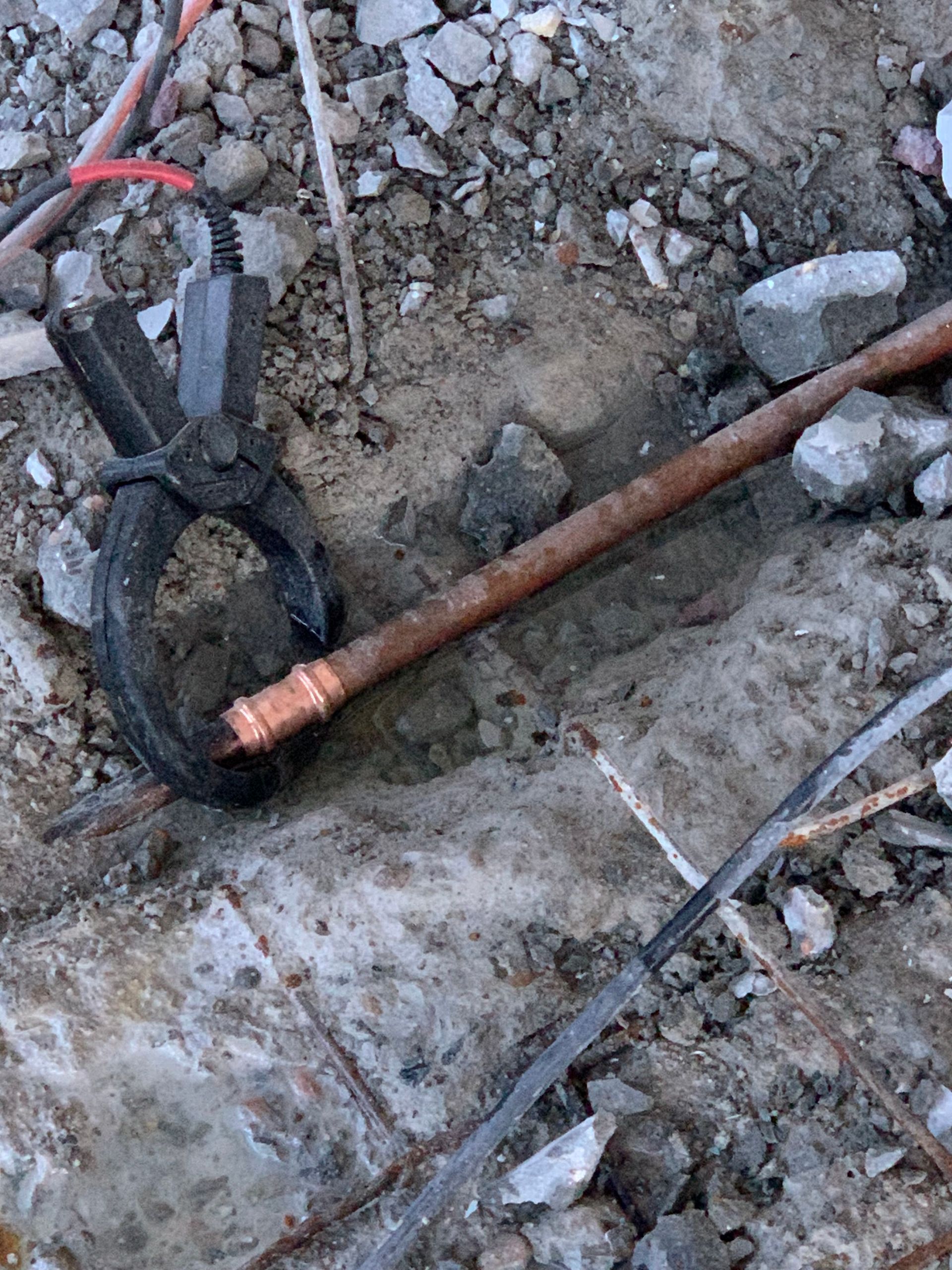 A copper pipe is laying on the ground next to a pair of pliers.