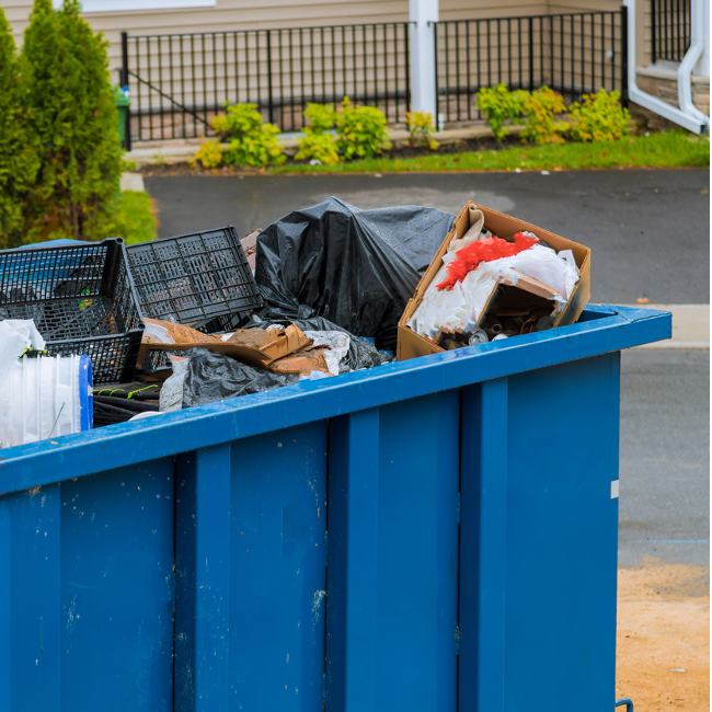 A blue dumpster filled with trash and a santa hat.