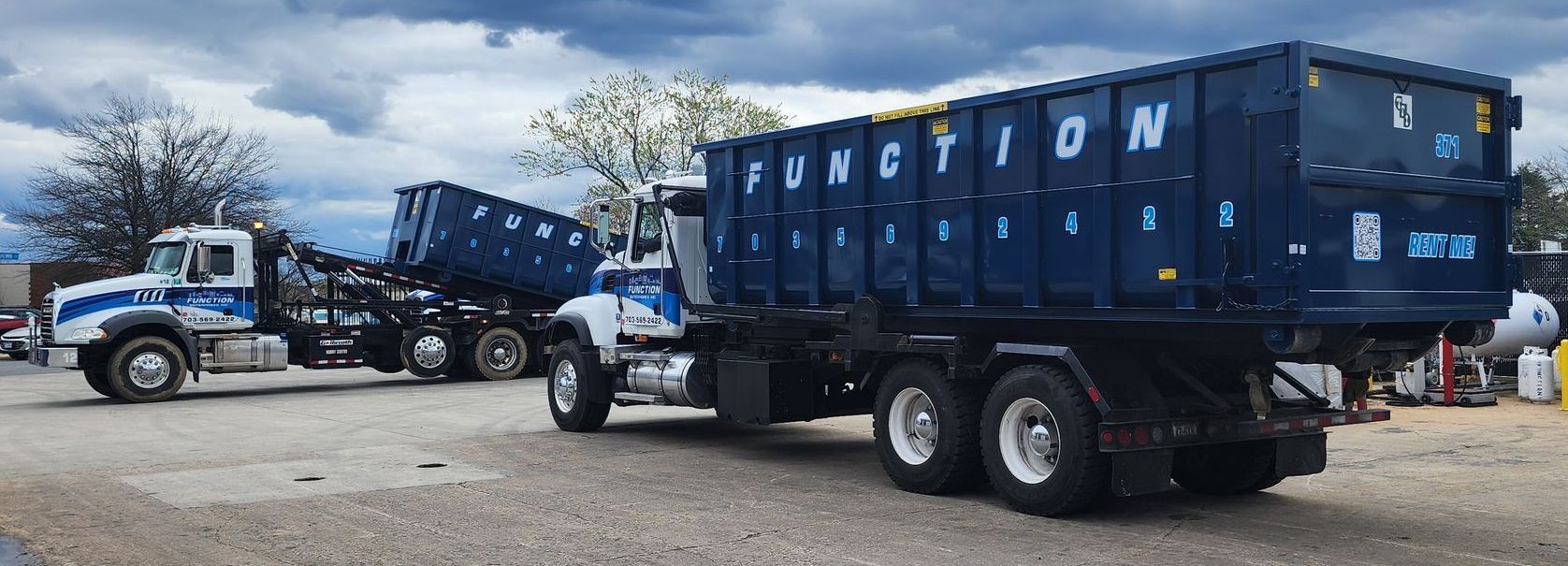 Two Function roll off dump trucks are parked next to each other in a gravel lot.