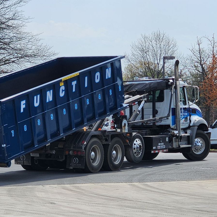 A Function dumpster is being towed by a truck in a parking lot.
