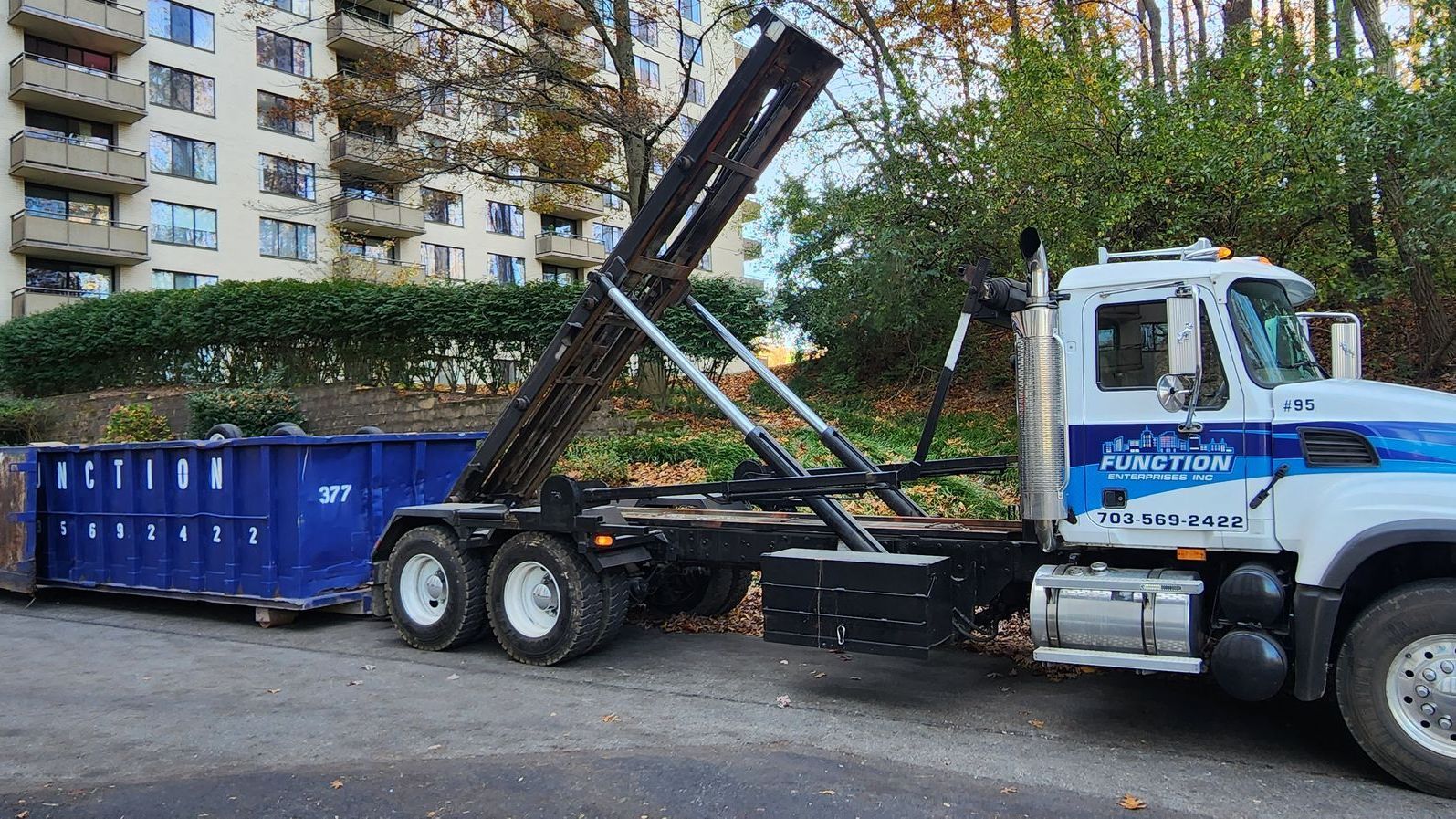 A dump truck with a blue dumpster attached to it is parked on the side of the road.