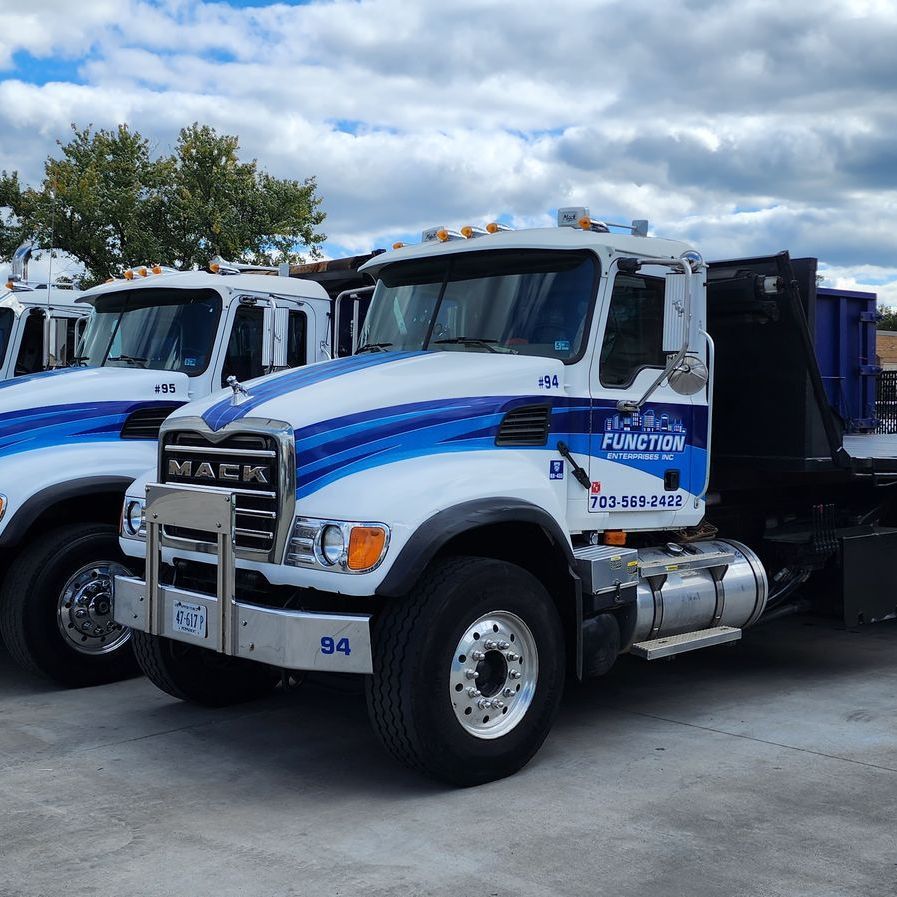 Function roll-off trucks are parked next to each other in a parking lot.