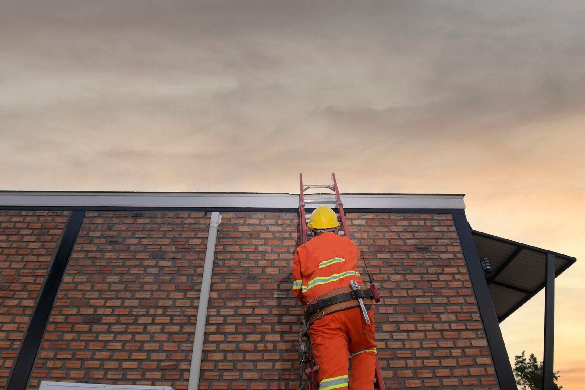 A Construction worker is climbing a ladder on top of a brick building.