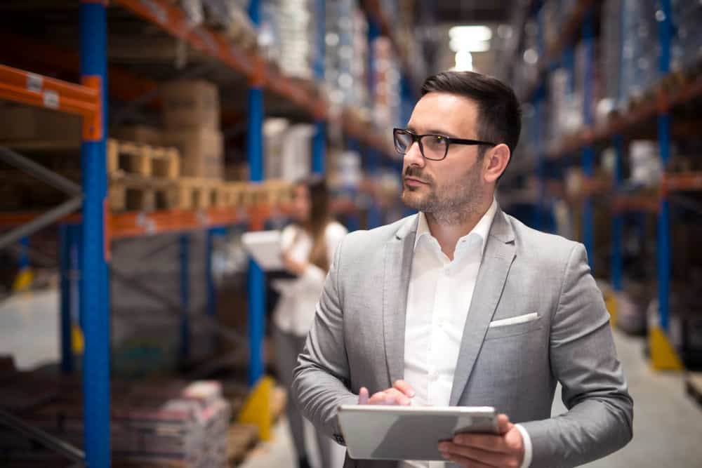 a man in a suit is holding a tablet in a warehouse .