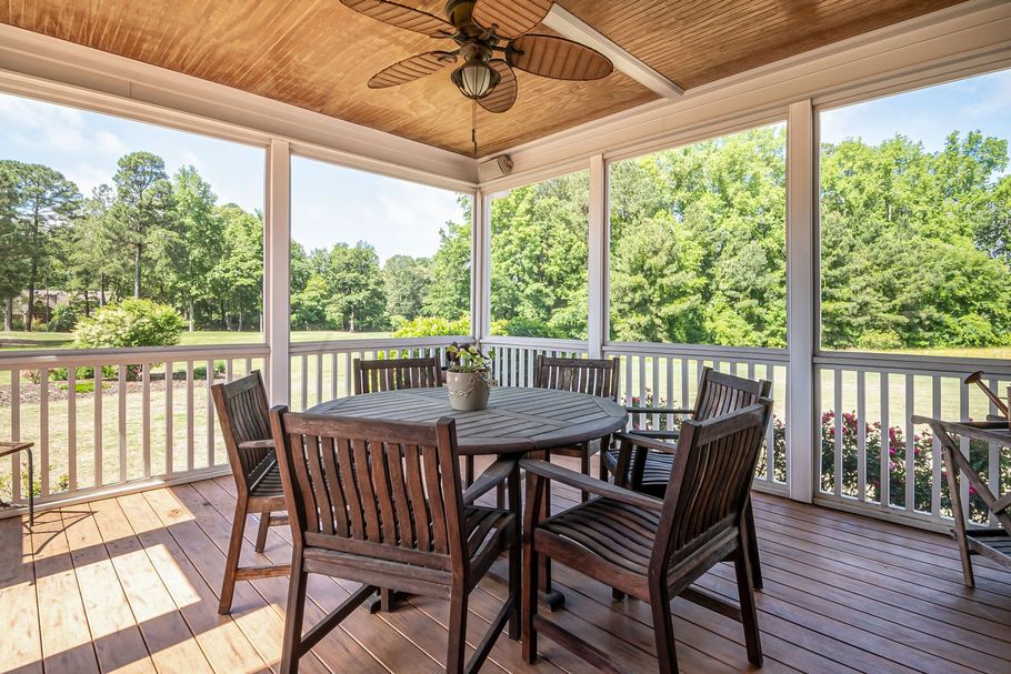 Covered wooden deck with wicker chairs and table overlooking a green yard and trees