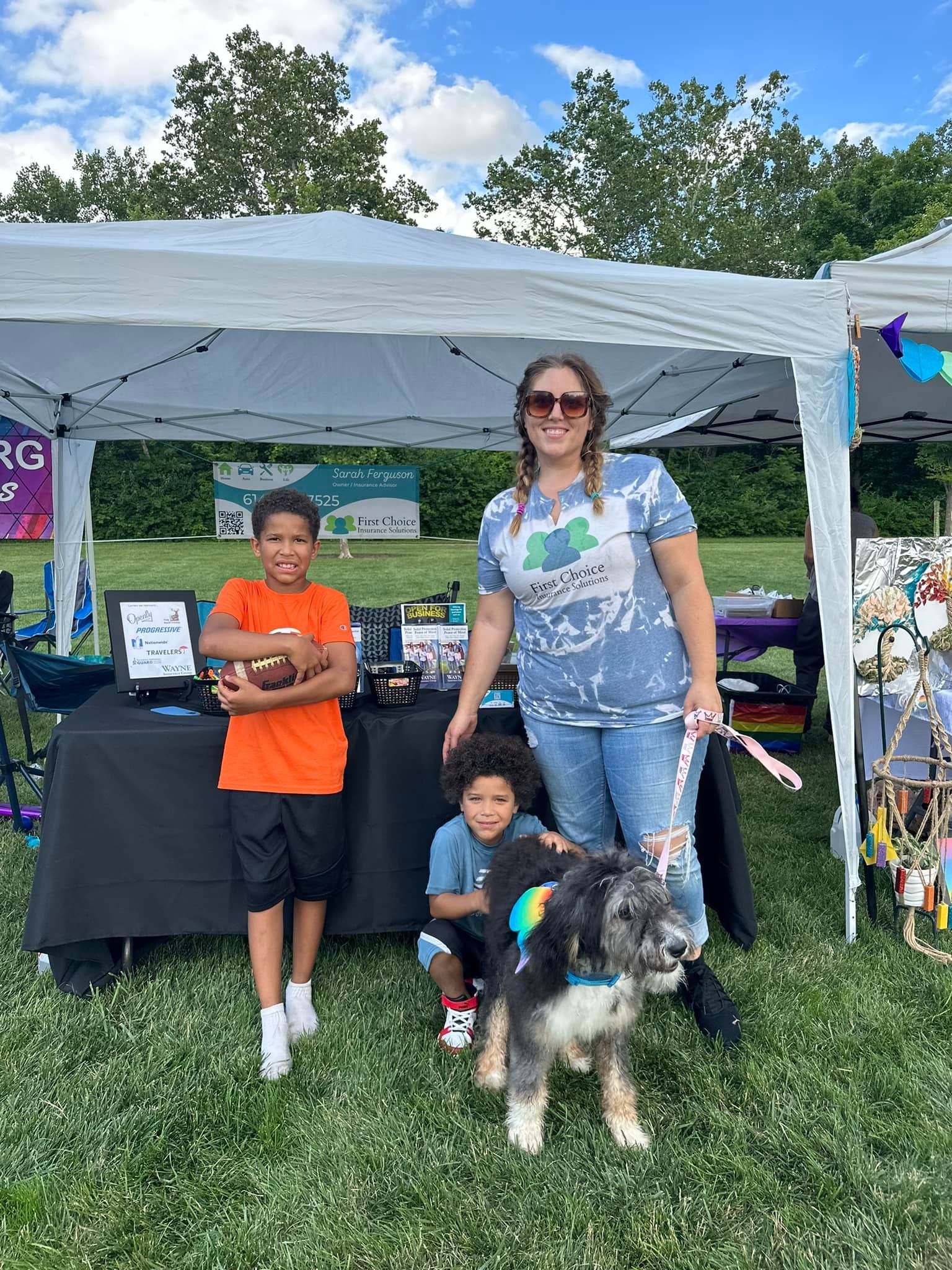 A woman and two children are standing next to a dog in front of a tent.